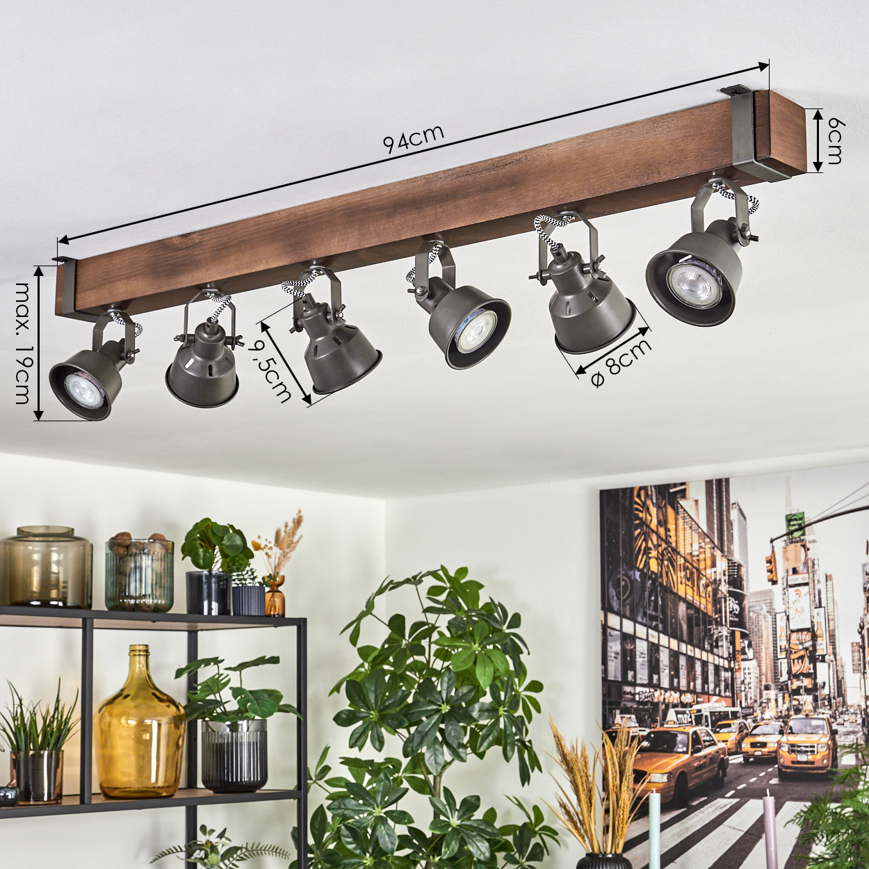Deckenstrahler mit sechs dunkelgrauen Lampen auf einem braunen Holzbalken. Pflanzen und ein New York City Foto im Hintergrund.