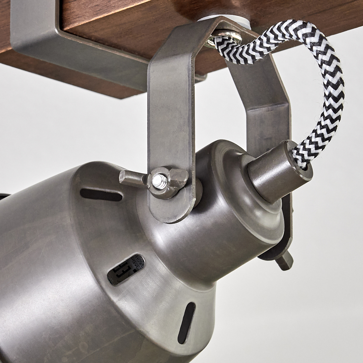 Ein Metallscheinwerfer ist mit einer Halterung an einer Holzoberfläche befestigt. Das Kabel ist schwarz und weiß. Der Hintergrund ist weiß.