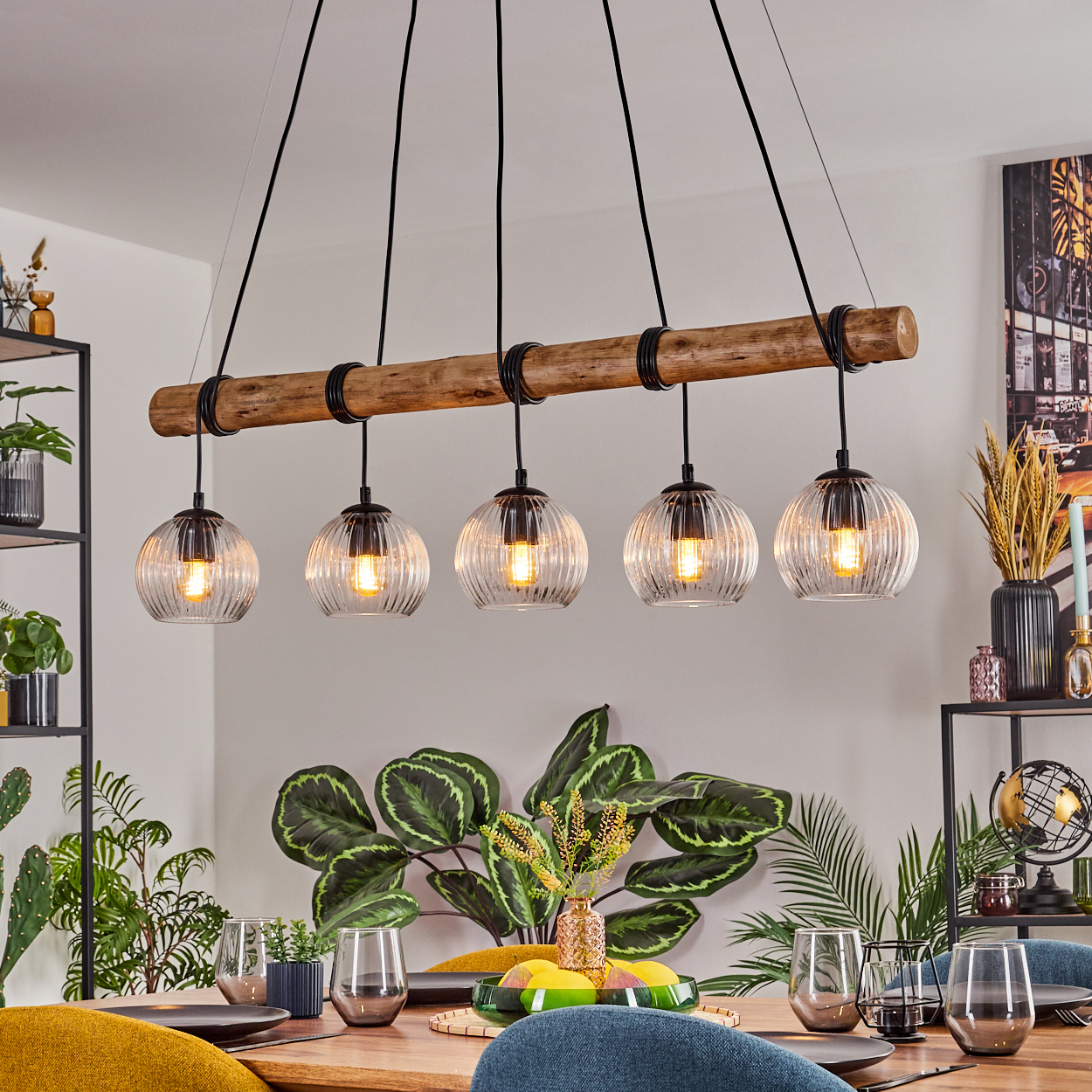 Ein Esszimmer mit Holztisch, Deckenleuchte mit fünf Glaslampen und grünen Pflanzen. Der Tisch ist gedeckt.
