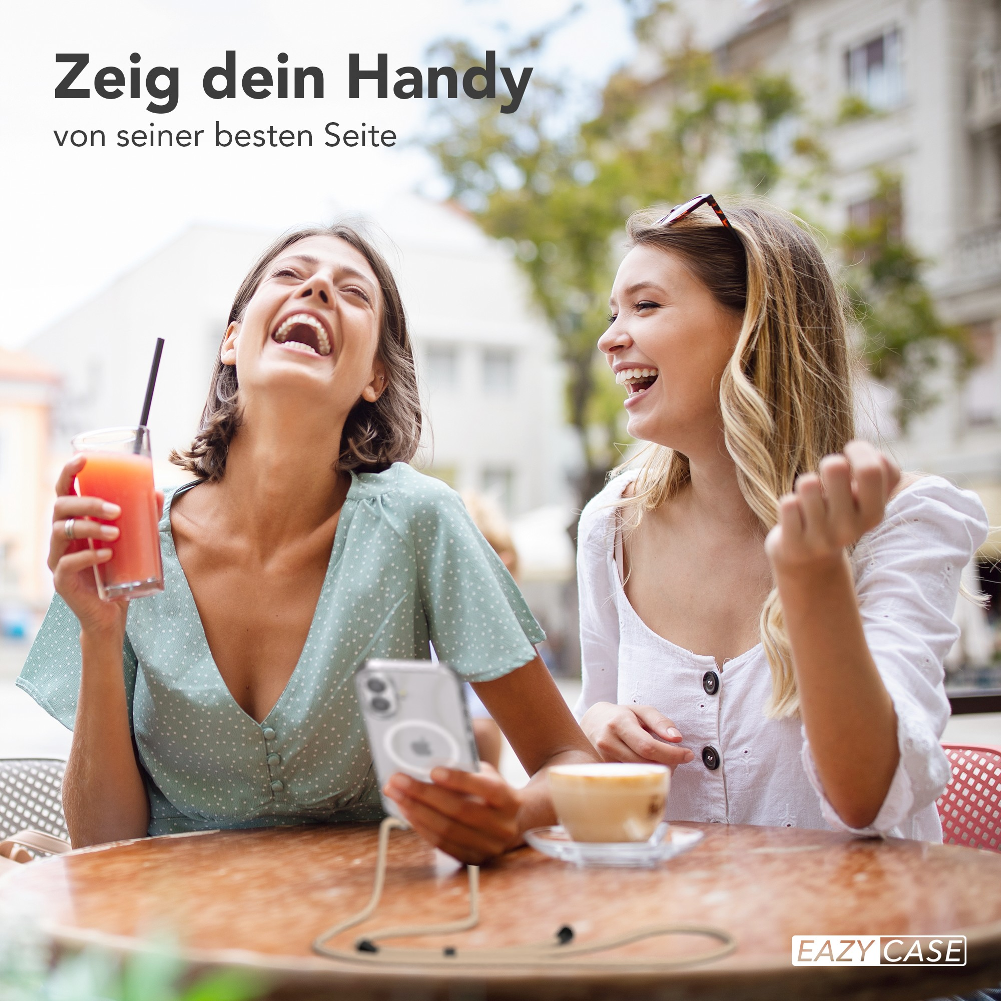 Zwei lachende Frauen in einem Café. Eine hält ein Getränk, die andere ein Telefon. Eine Kaffeetasse steht auf dem Tisch.