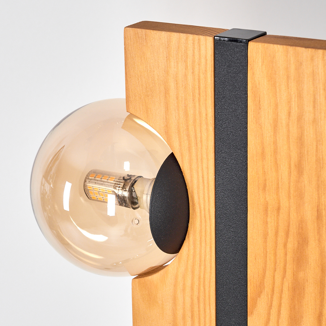 Nahaufnahme einer Holzlampe mit einer runden, bernsteinfarbenen Glühbirne. Die Lampe hat einen schwarzen Metallstreifen und einen weißen Hintergrund.