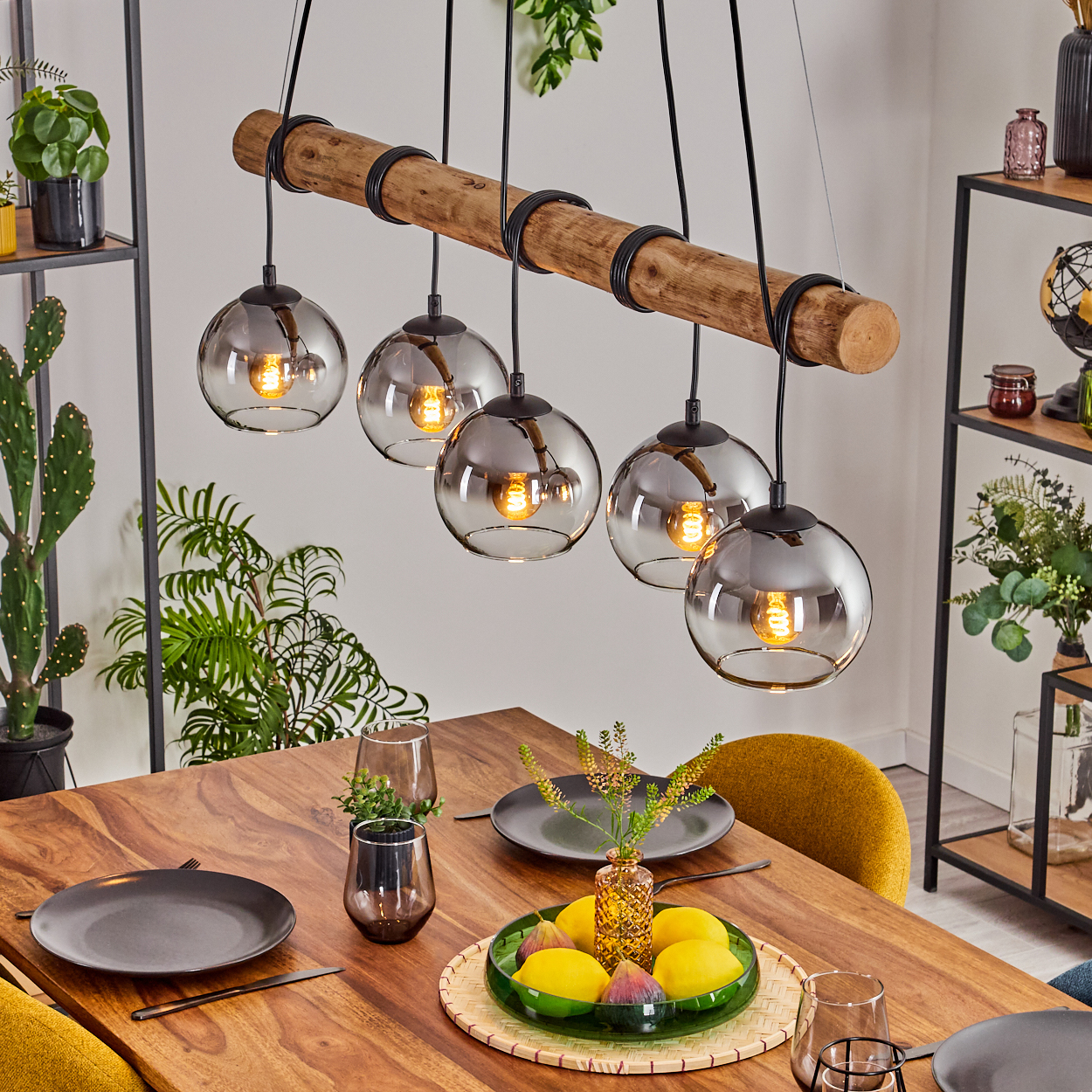 Esszimmer mit Holztisch, Hängelampen und Tischdeko mit Obst und Tellern.
