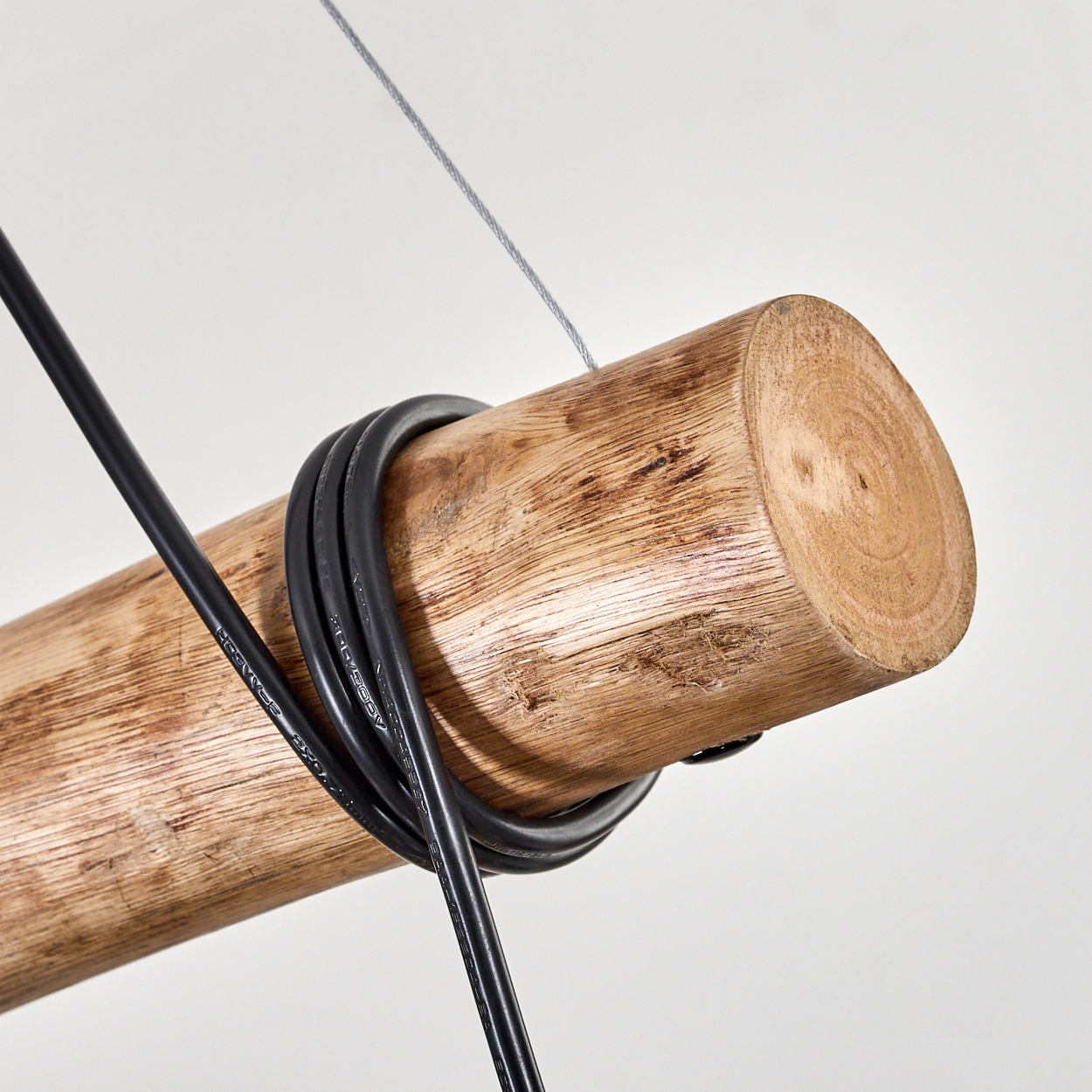Nahaufnahme eines Holzstamms mit einem schwarzen Kabel darum. Ein dünner Draht hängt von oben.
