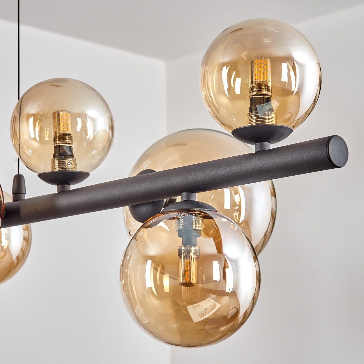 Eine moderne Deckenleuchte mit mehreren kugelförmigen, bernsteinfarbenen Glasschirmen, einem schwarzen Metallrahmen und sichtbaren Glühbirnen.
