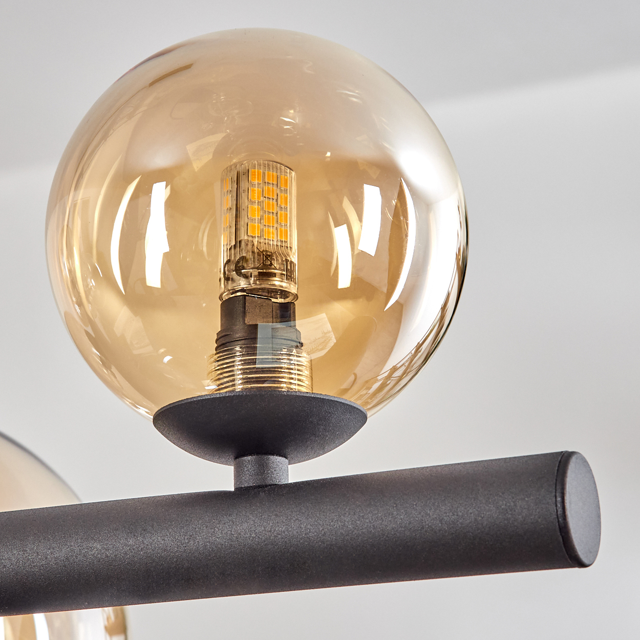Nahaufnahme einer modernen Leuchte. Ein runder, bernsteinfarbener Glasschirm umgibt eine LED-Glühbirne. Die Leuchte hat eine schwarze Metallstange.