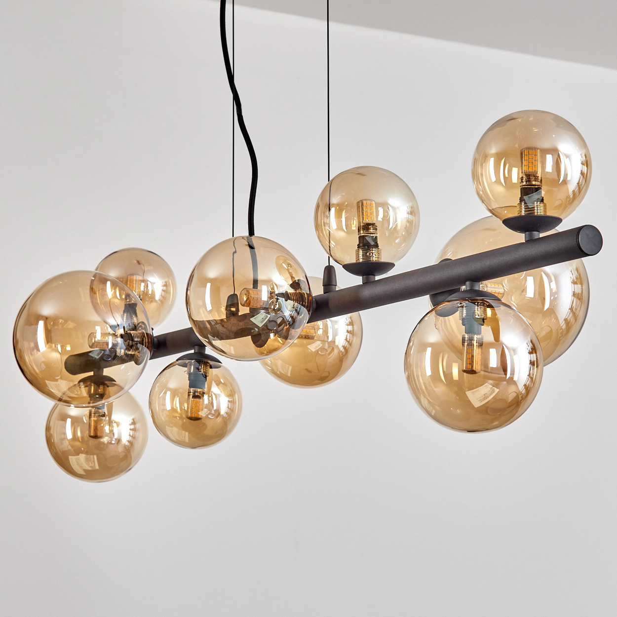 Eine moderne Deckenleuchte mit mehreren bernsteinfarbenen Glaskugeln und dunklen Metallarmen, die vor weißem Hintergrund von der Decke hängt.