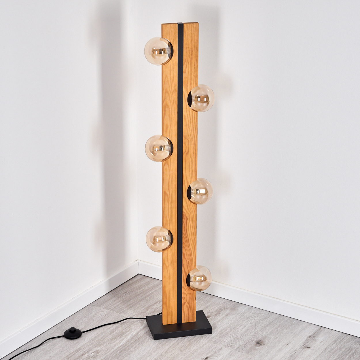 Eine moderne Holz-Stehlampe mit sechs kugelförmigen Glühbirnen. Die Lampe steht hoch in einer Ecke, mit schwarzem Sockel und Schalter.