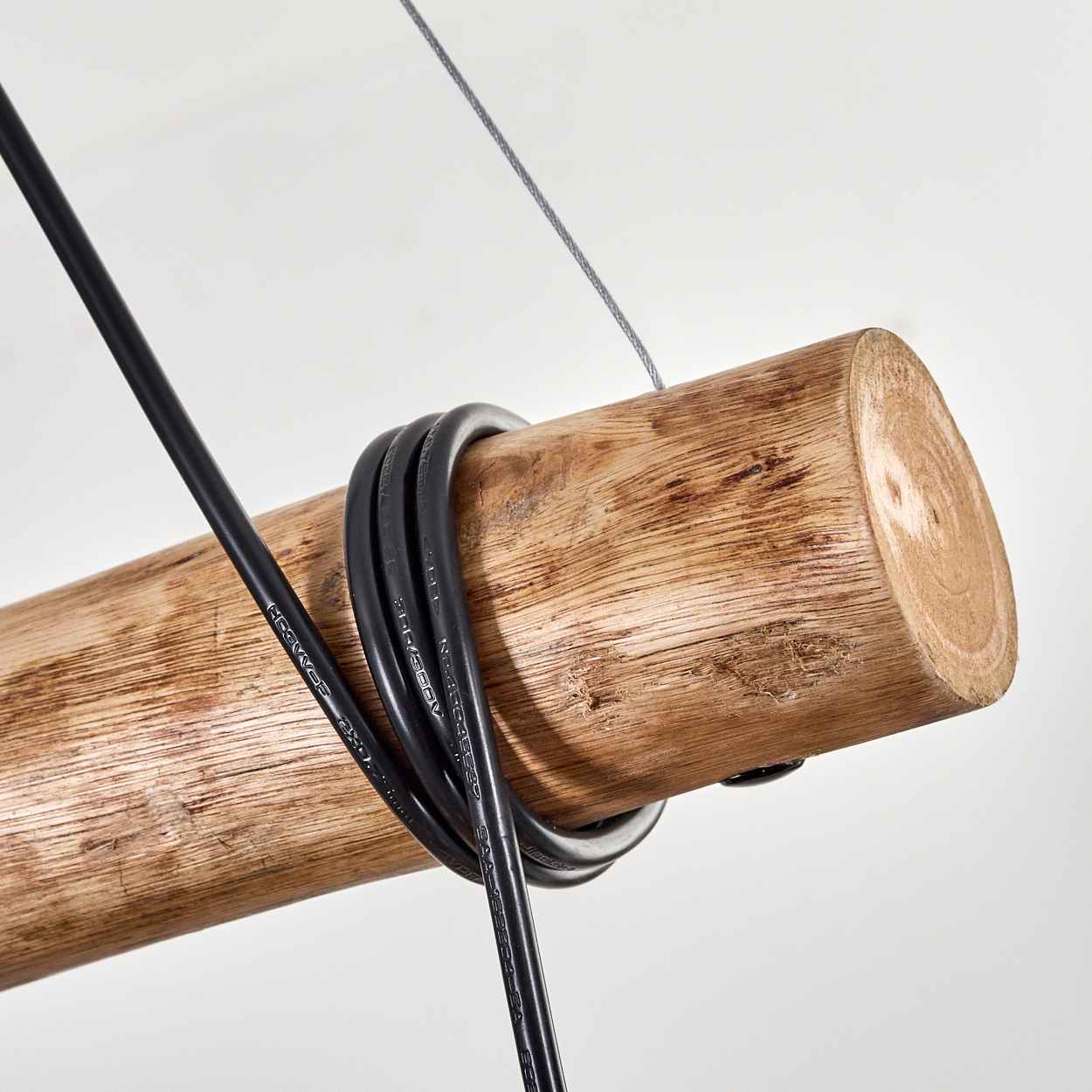 Nahaufnahme eines Holzbalkens mit einem schwarzen Kabel darum und einem dünnen Draht darüber, alles vor weißem Hintergrund.