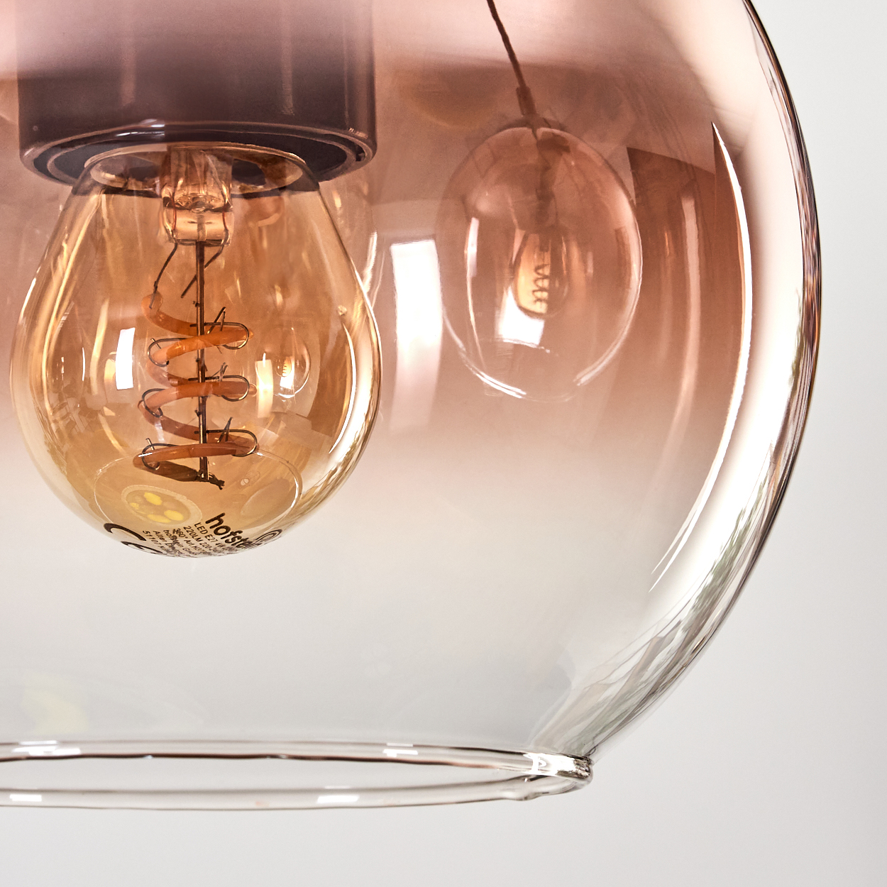 Nahaufnahme einer Glas-Pendelleuchte. Die Leuchte hat eine große Glühbirne, einen Wendelfaden und einen transparenten Farbverlauf.
