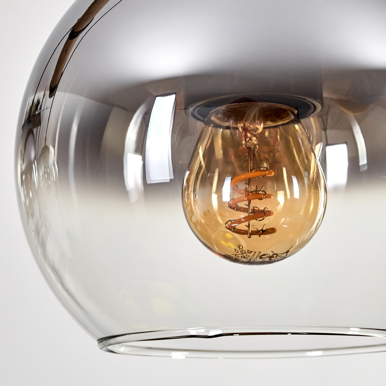 Nahaufnahme einer Glasleuchte, eine Glühbirne mit Spiralfaden im Inneren. Das Glas ist klar und der Hintergrund ist weiß.