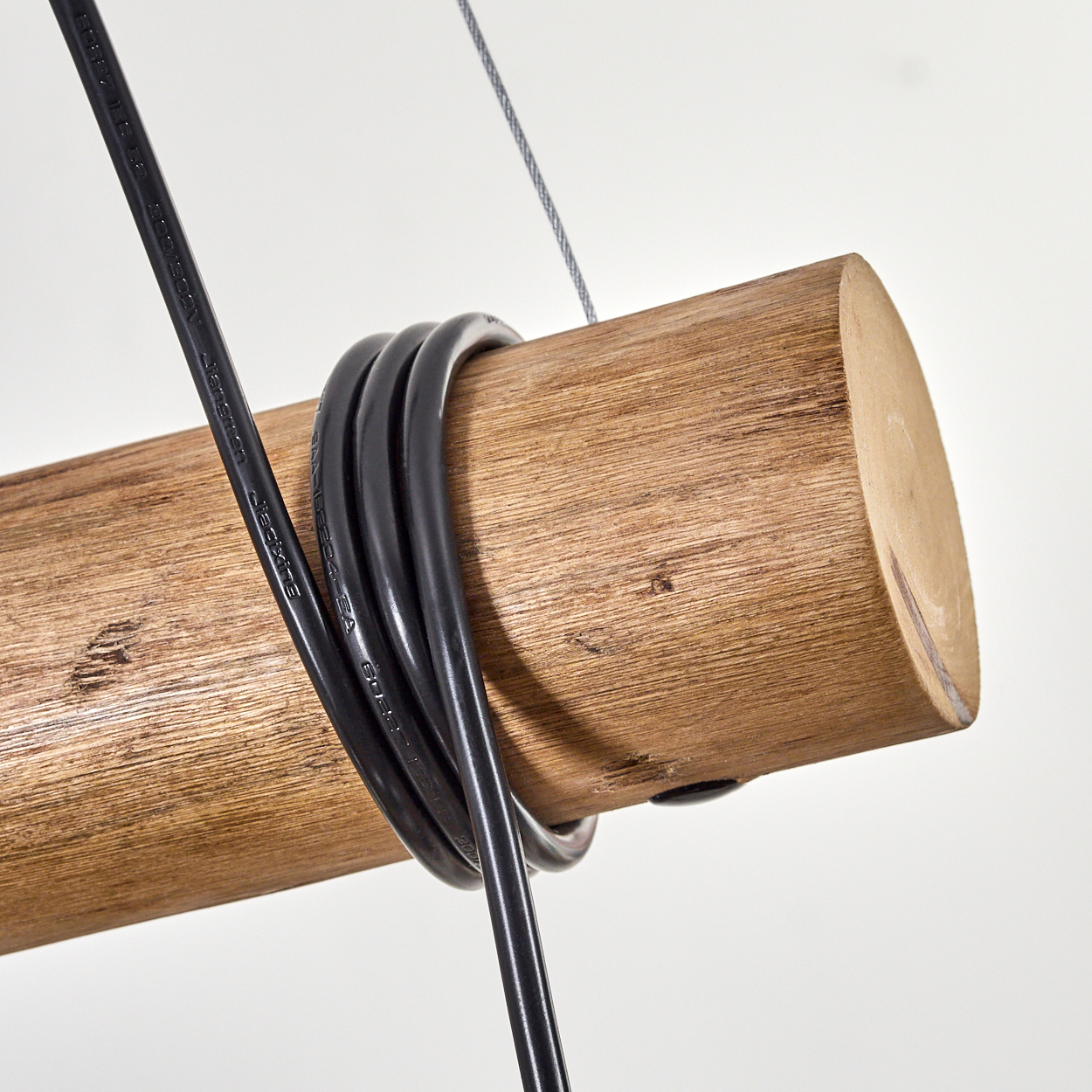 Nahaufnahme eines Holzbalkens mit schwarzem Kabel. Ein Kabel hängt von der Decke.