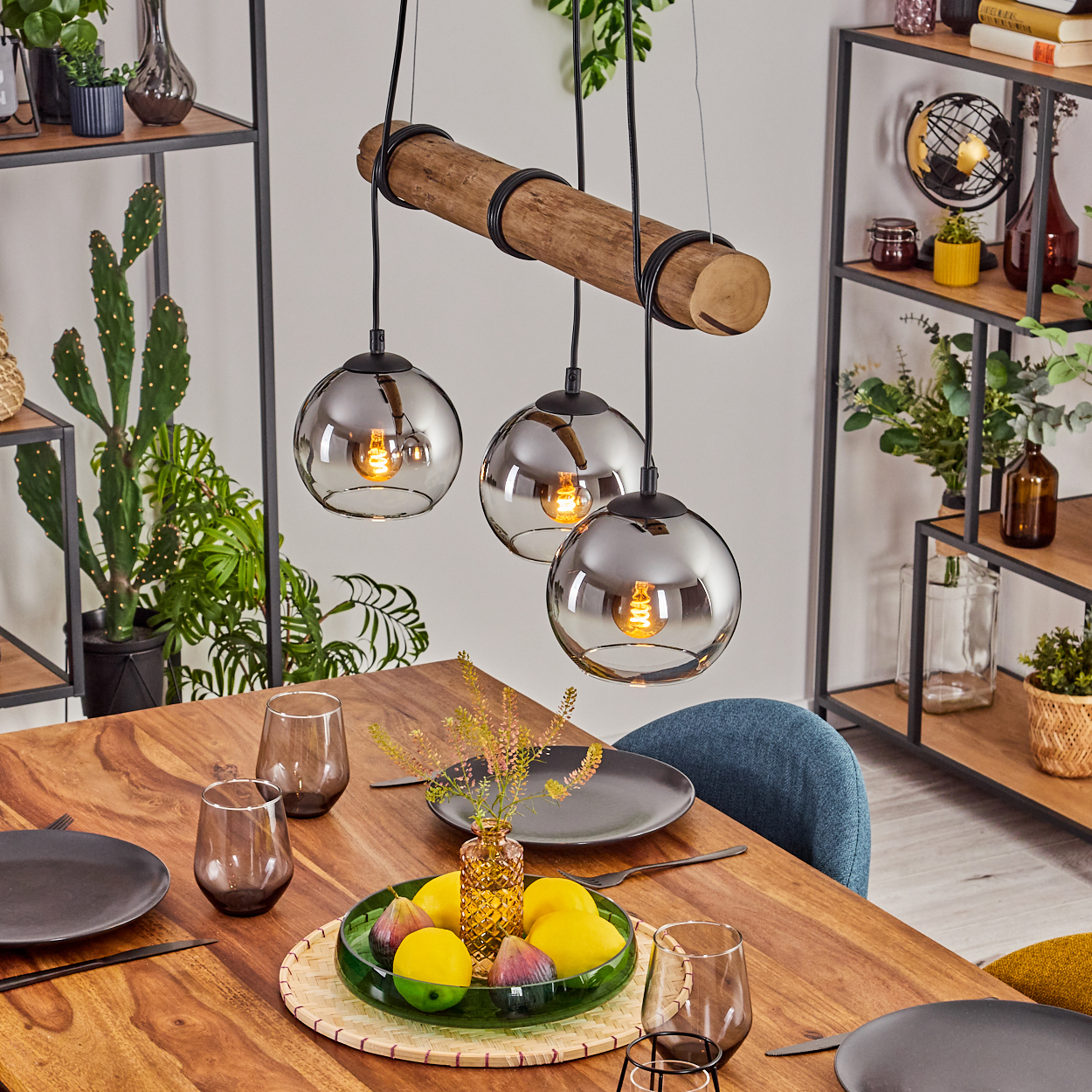 Esszimmer mit Holztisch, Glaslampen und Obstteller. Regale mit Pflanzen und Dekoration im Hintergrund.