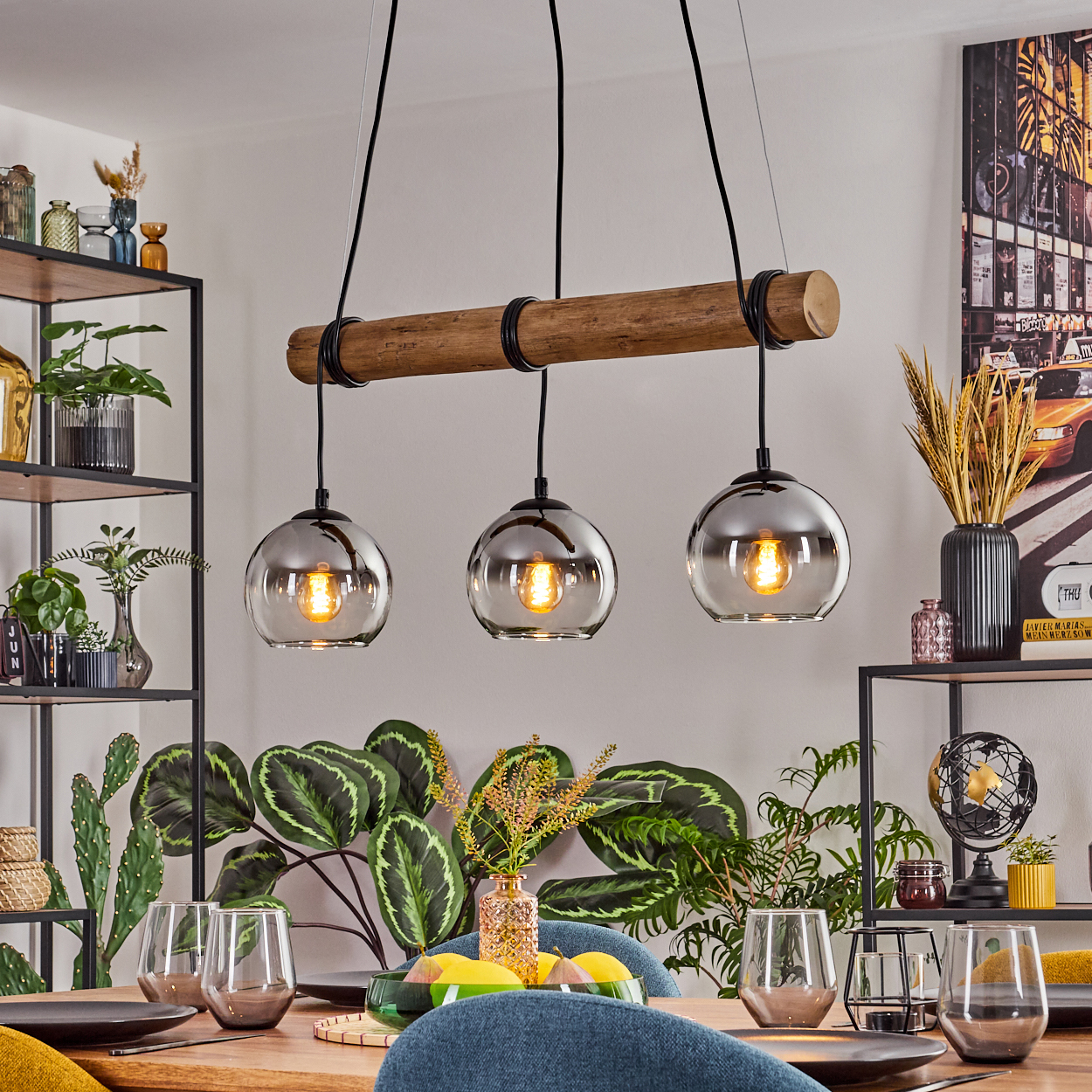 Esszimmer mit Holzbalken-Leuchte, drei Glaslampen, Tisch mit Gläsern und Tellern, Pflanzen und Dekorationen.