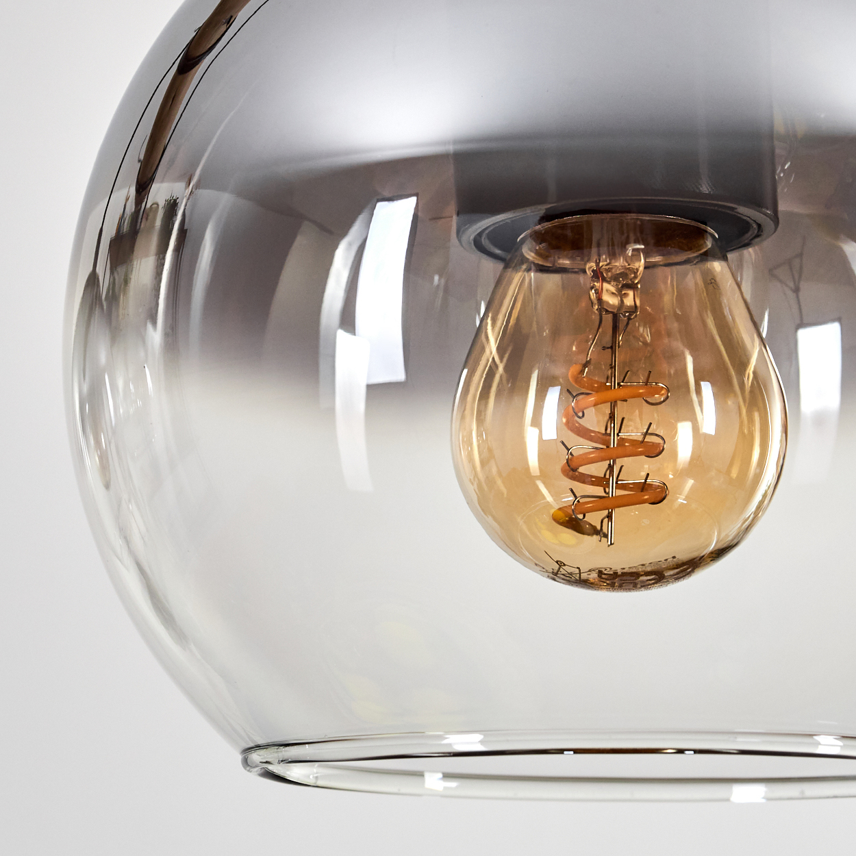 Nahaufnahme einer Leuchte mit klarem Glasschirm und einer sichtbaren Edison-Glühbirne mit Spiralfaden.