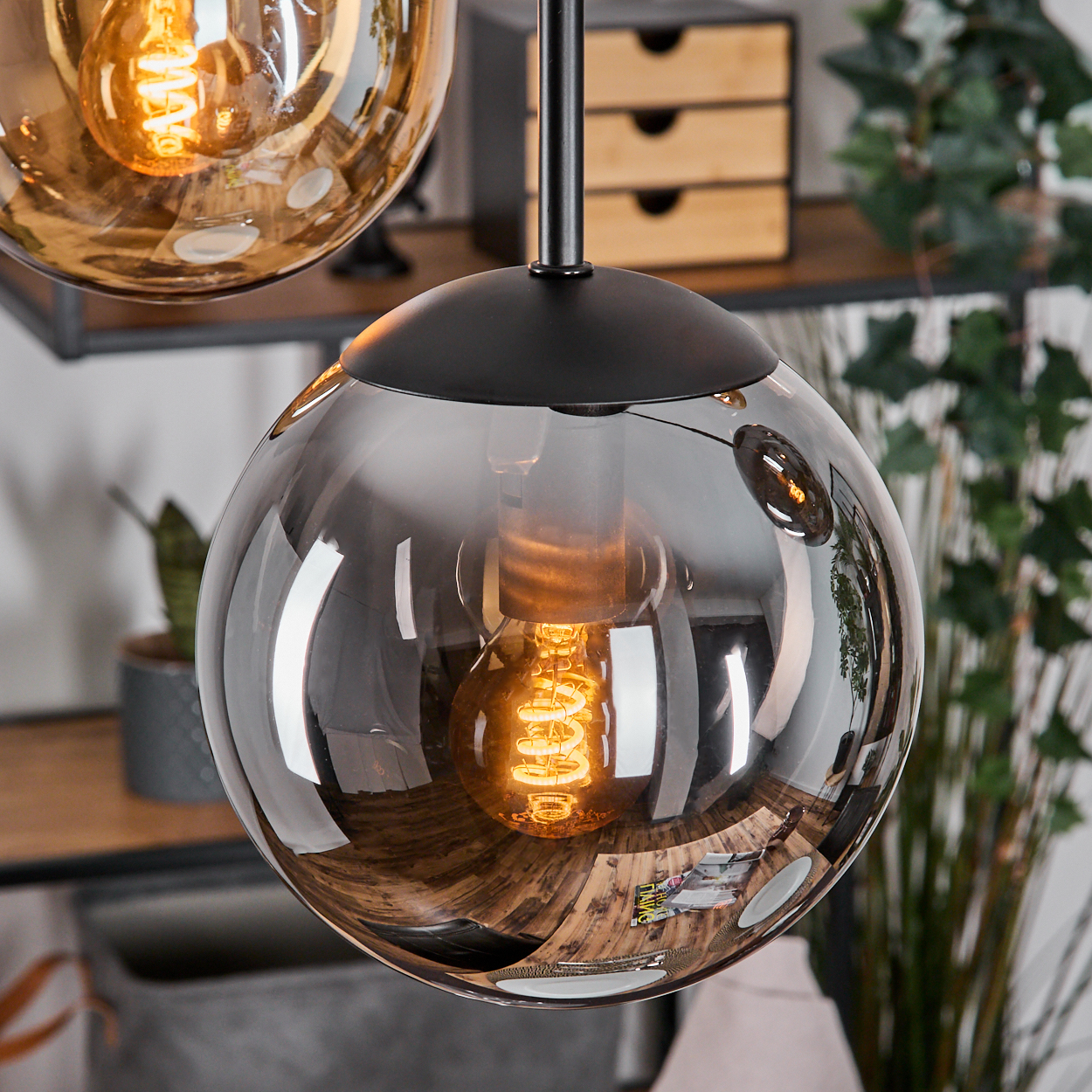 Nahaufnahme einer modernen Pendelleuchte mit kugelförmigem Glasschirm und sichtbarer, leuchtender Glühbirne.