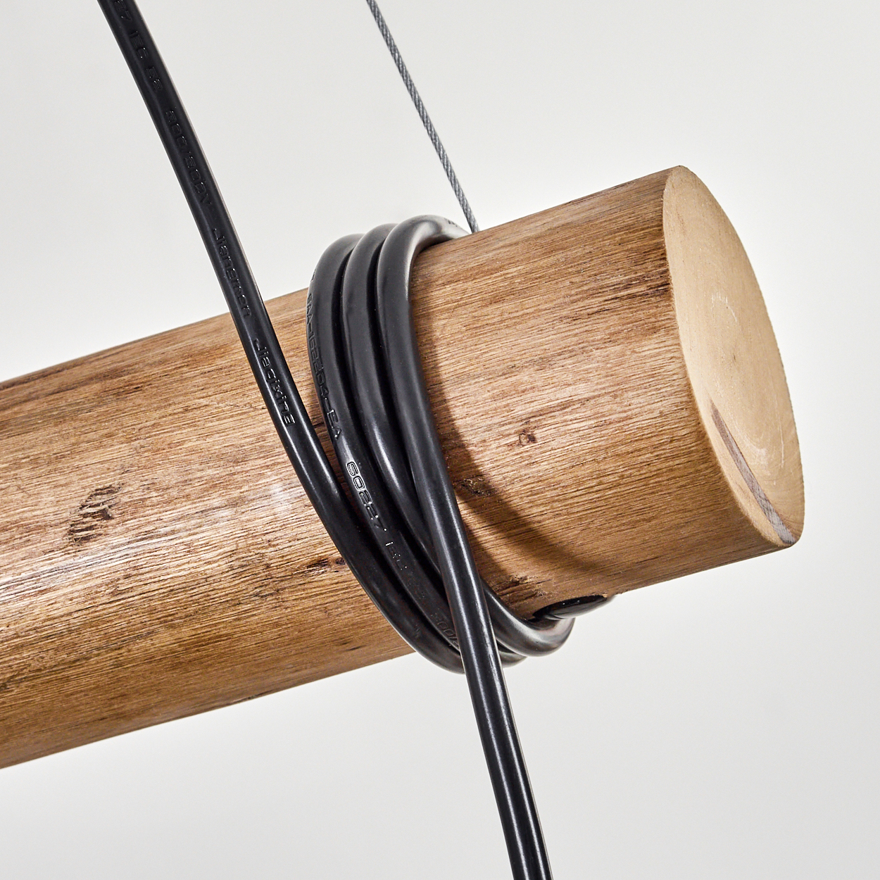 Nahaufnahme eines Holzbalkens mit schwarzen Kabeln. Ein silbernes Kabel hängt darüber, vor weißem Hintergrund.