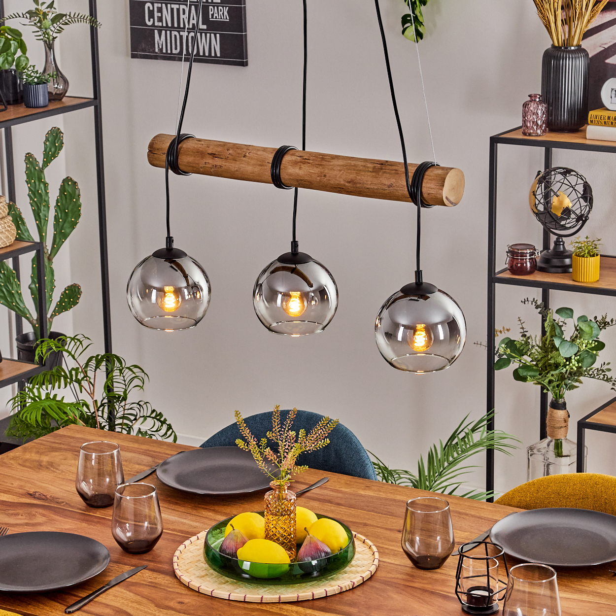 Esszimmer mit Holztisch, Hängelampen und Dekoration. Enthält Gläser, Teller, Zitronen und Pflanzen. Der Hintergrund hat Regale.