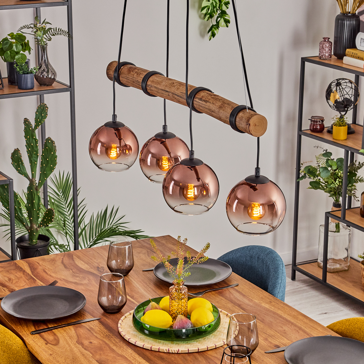 Ein Esszimmer mit Holztisch, Hängelampen und Regalen. Der Tisch hat Teller, Gläser und eine Obstschale. Pflanzen schmücken den Raum.