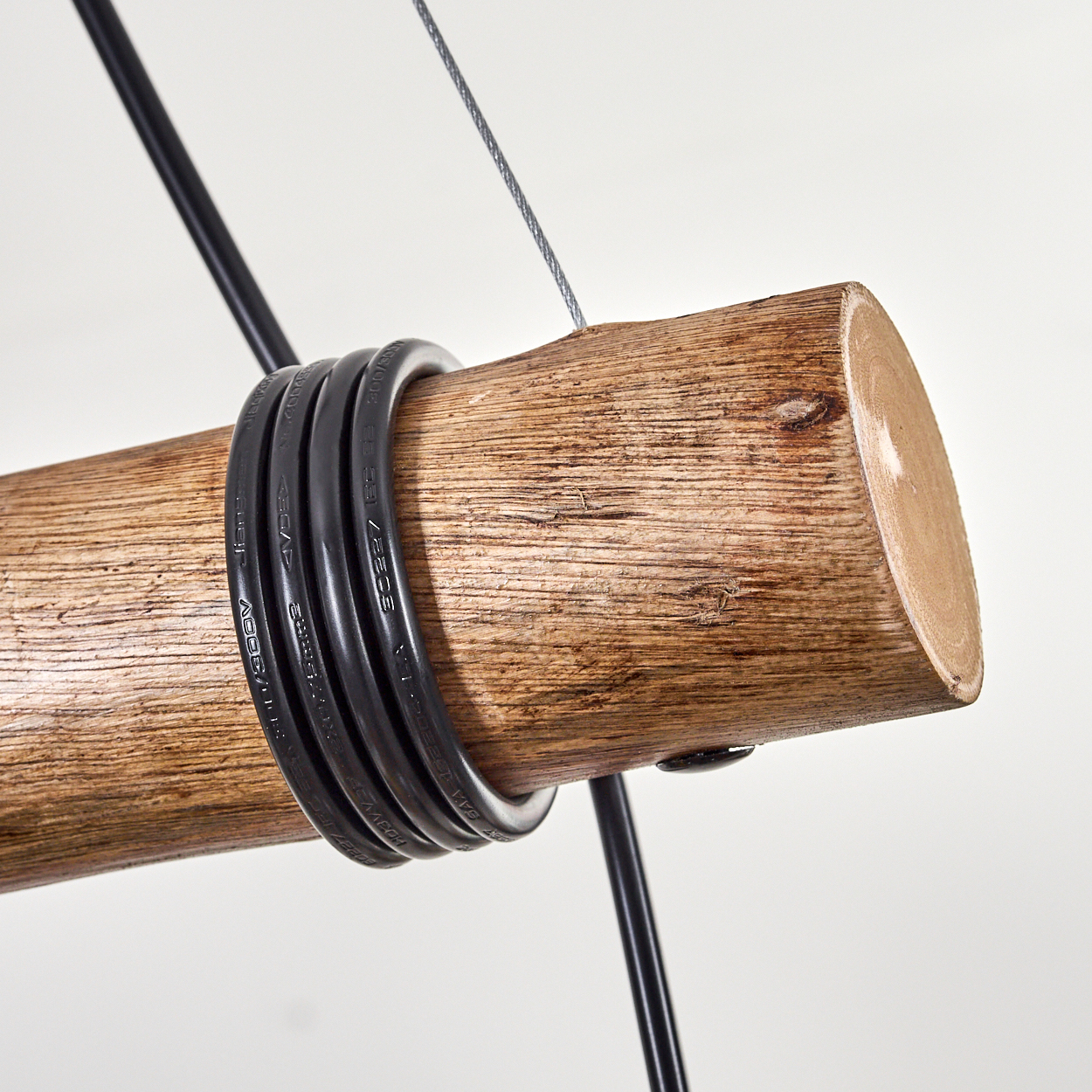 Nahaufnahme eines Holzbalkens mit schwarzen Drähten. Ein Metallkabel und schwarze Drähte sind sichtbar.