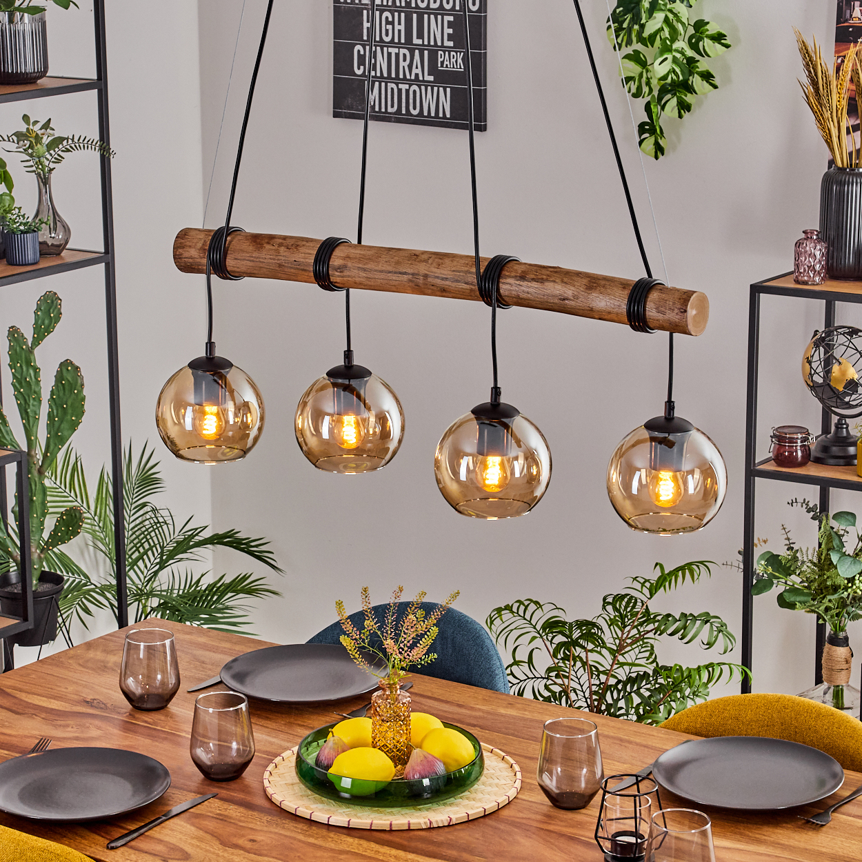 Esszimmer mit Holztisch, vier Kugellampen und Obstplatte. Pflanzen und Regale sind im Hintergrund zu sehen.
