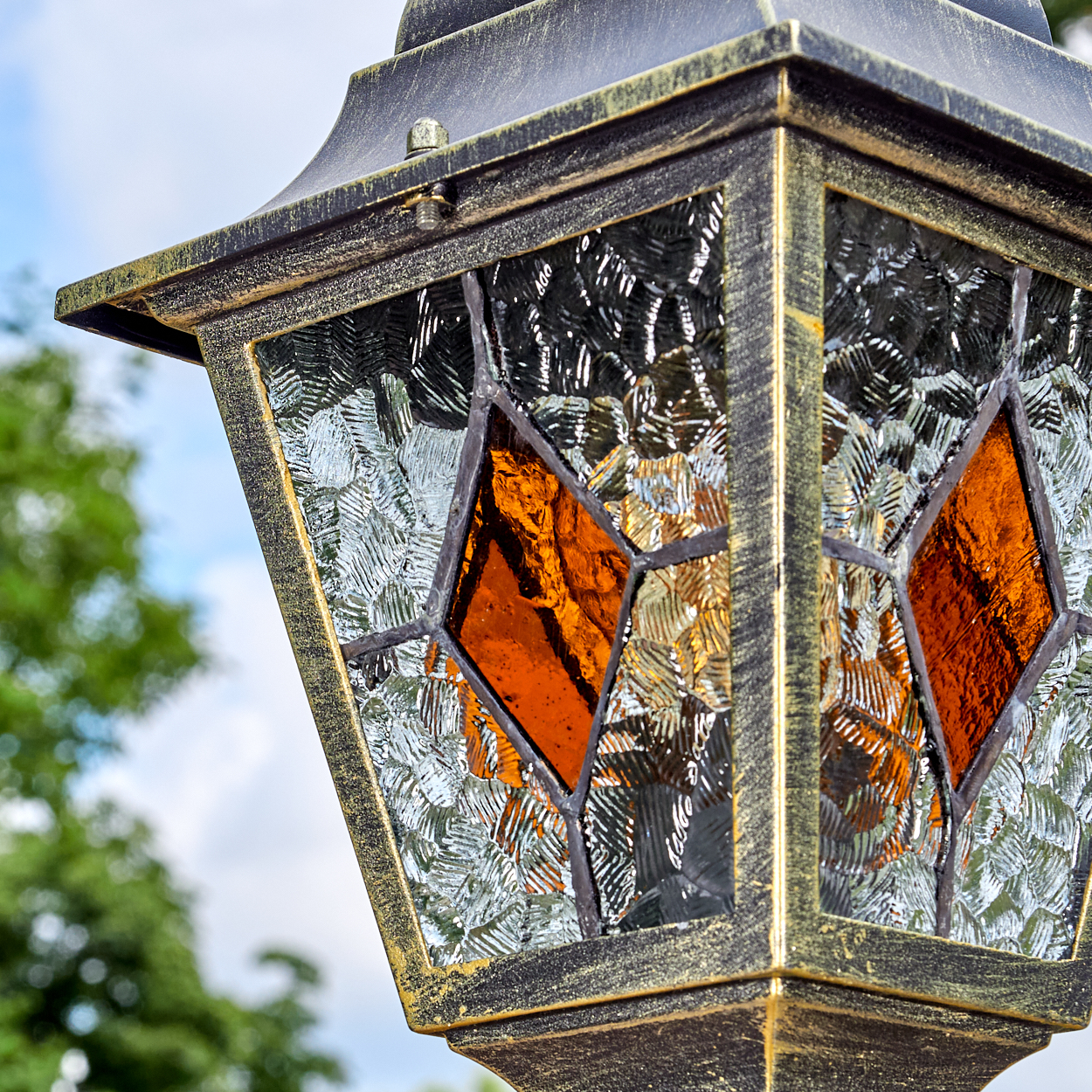 Nahaufnahme einer dekorativen Außenlampe mit strukturiertem Glas und bernsteinfarbenen rautenförmigen Einsätzen. Gold- und schwarzer Metallrahmen.