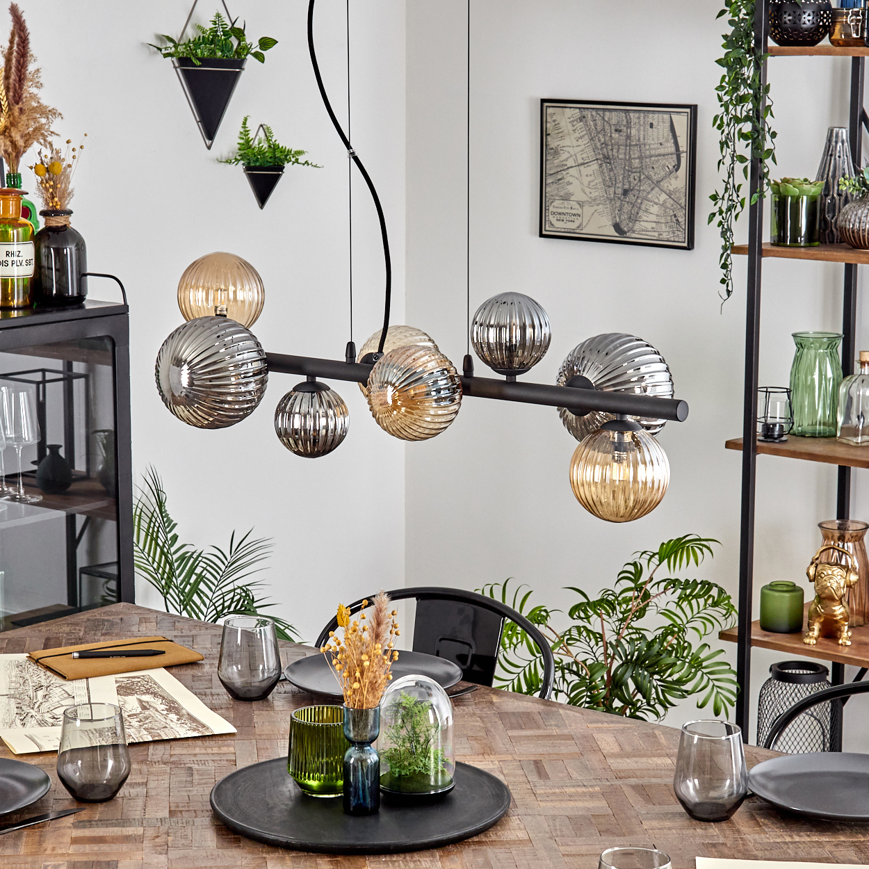 Ein Esszimmer mit Holztisch, modernem Kronleuchter mit Glaskugeln und dekorativen Pflanzen. Eine Karte und Dekoration an der Wand.