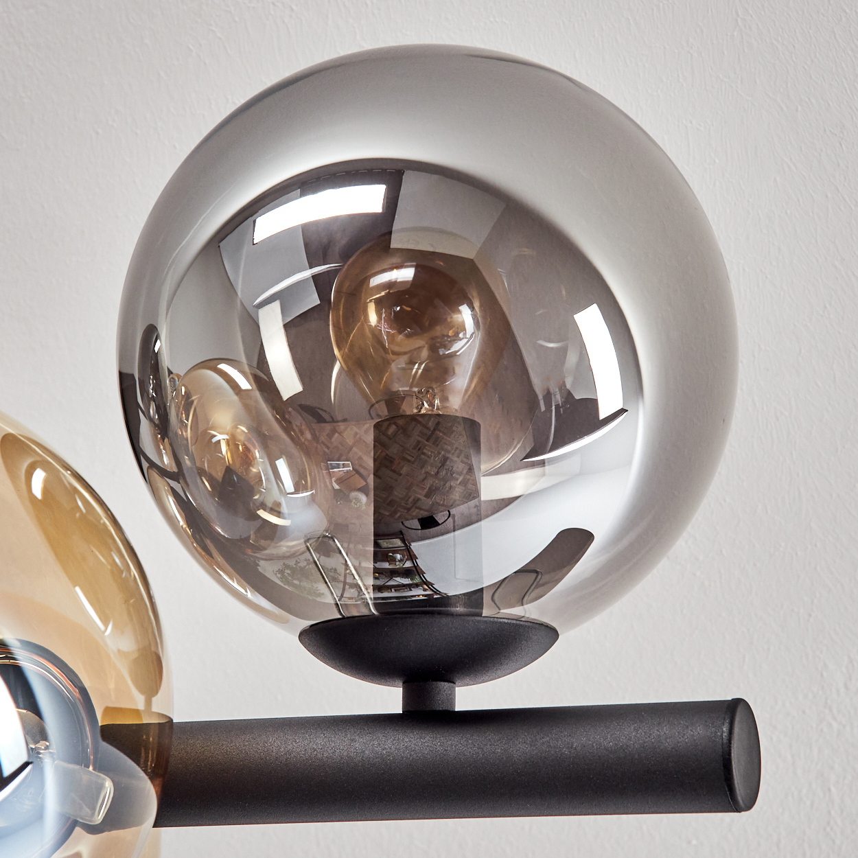 Nahaufnahme einer modernen Lampe mit drei Glaskugeln. Die mittlere Kugel ist grau und zeigt die Glühbirne. Schwarzer Metallarm.