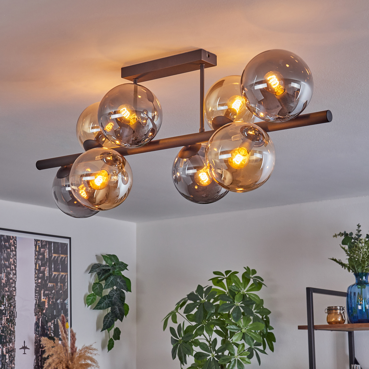 Moderne Deckenleuchte mit acht Glaskugelschirmen. Der Raum hat Pflanzen und ein Bild an der Wand. Das Licht ist an.