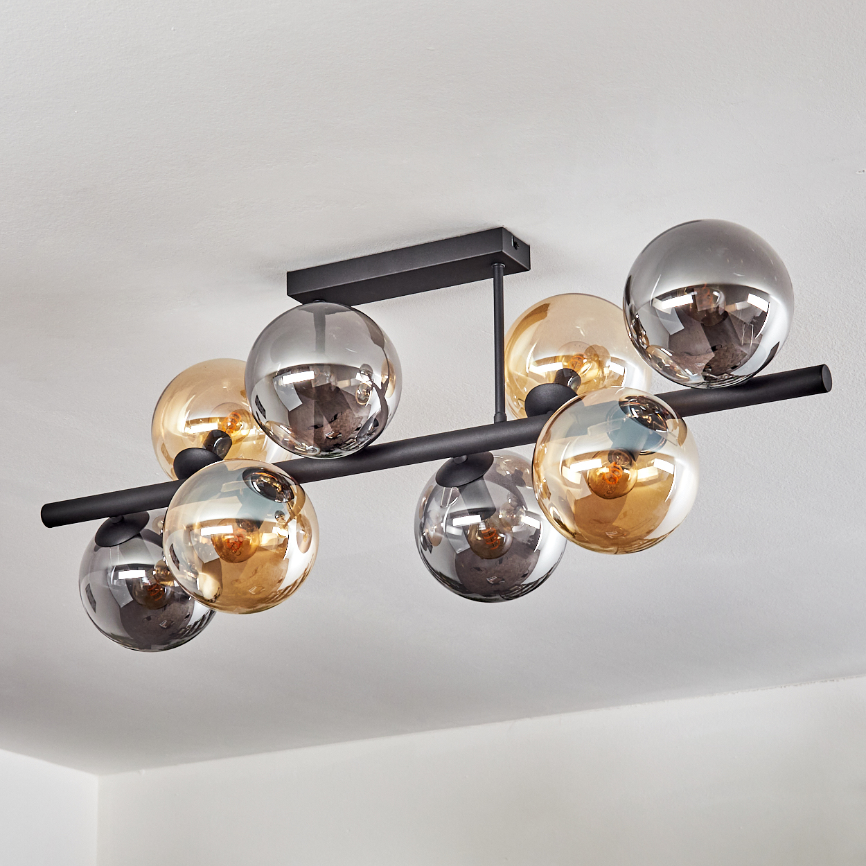Eine moderne Deckenleuchte mit kugelförmigen Glaskugeln in Gold und Silber, befestigt an einem schwarzen Metallrahmen.
