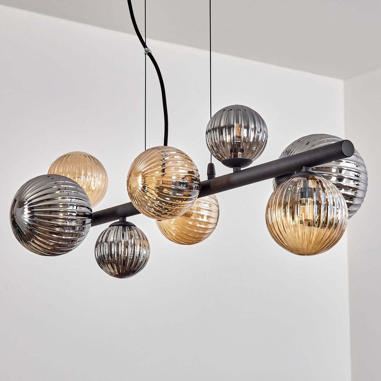 Eine moderne Deckenleuchte mit mehreren kugelförmigen Glaslampen in Silber- und Bernsteintönen, von der Decke abgehängt.