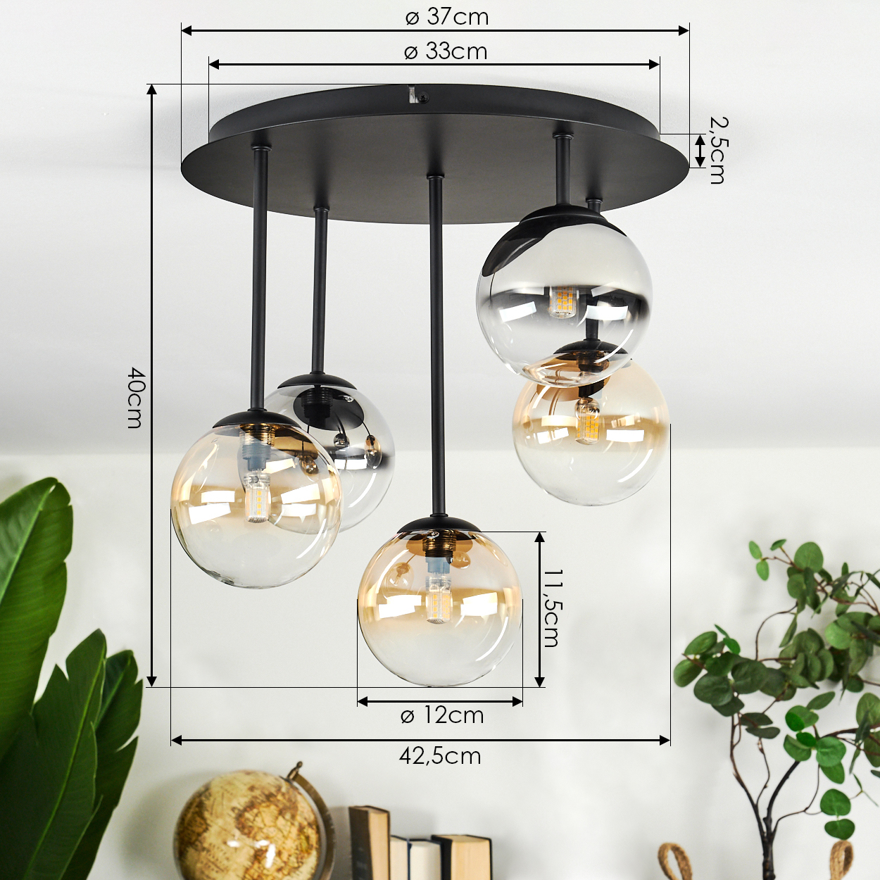 Eine moderne Deckenlampe mit fünf Glaskugeln, schwarzes Gestell. Abmessungen sind angegeben. Pflanzen und Dekorationen sind im Hintergrund.
