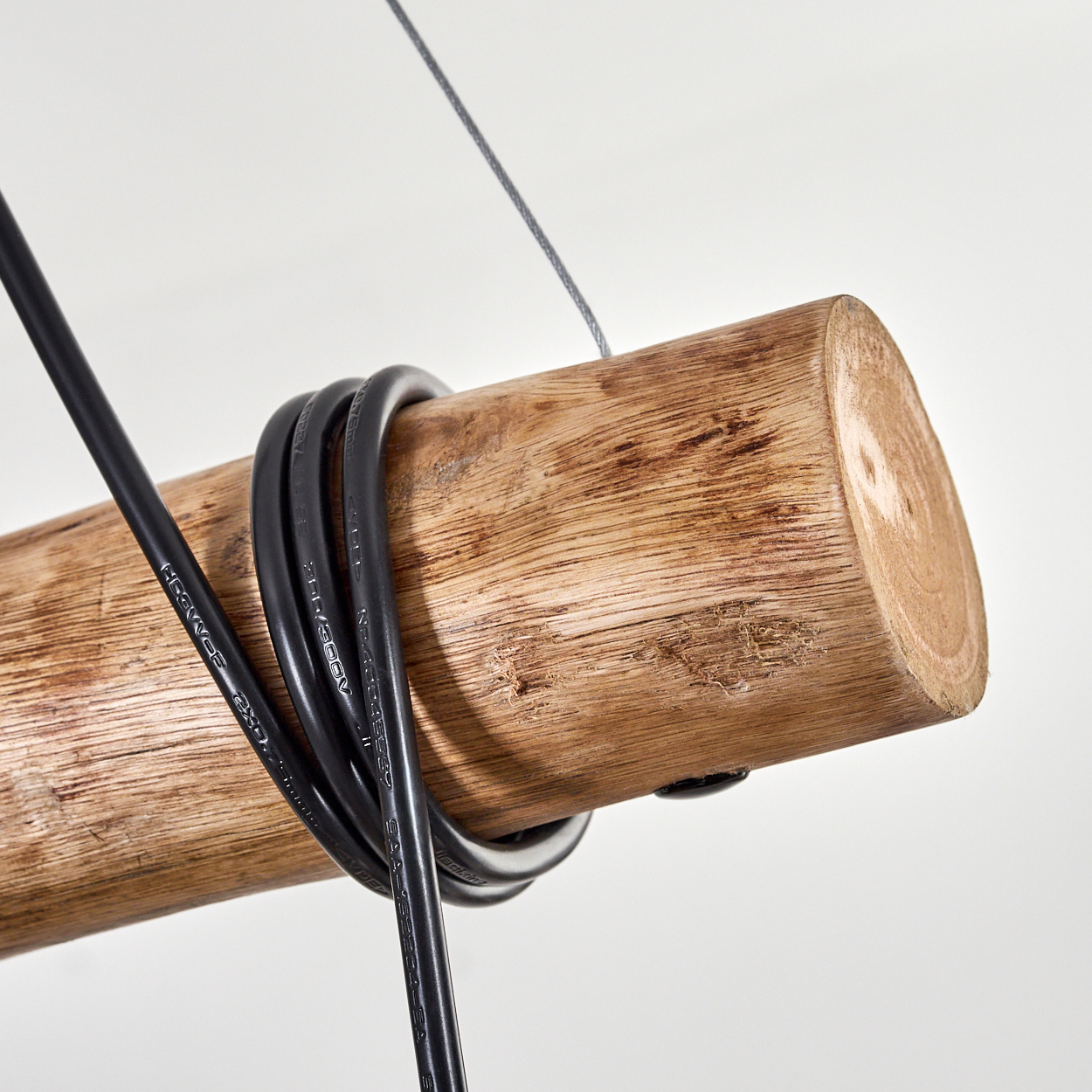 Ein Holzstamm mit schwarzen Kabeln, die darum gewickelt sind, an einem Draht vor weißem Hintergrund aufgehängt.