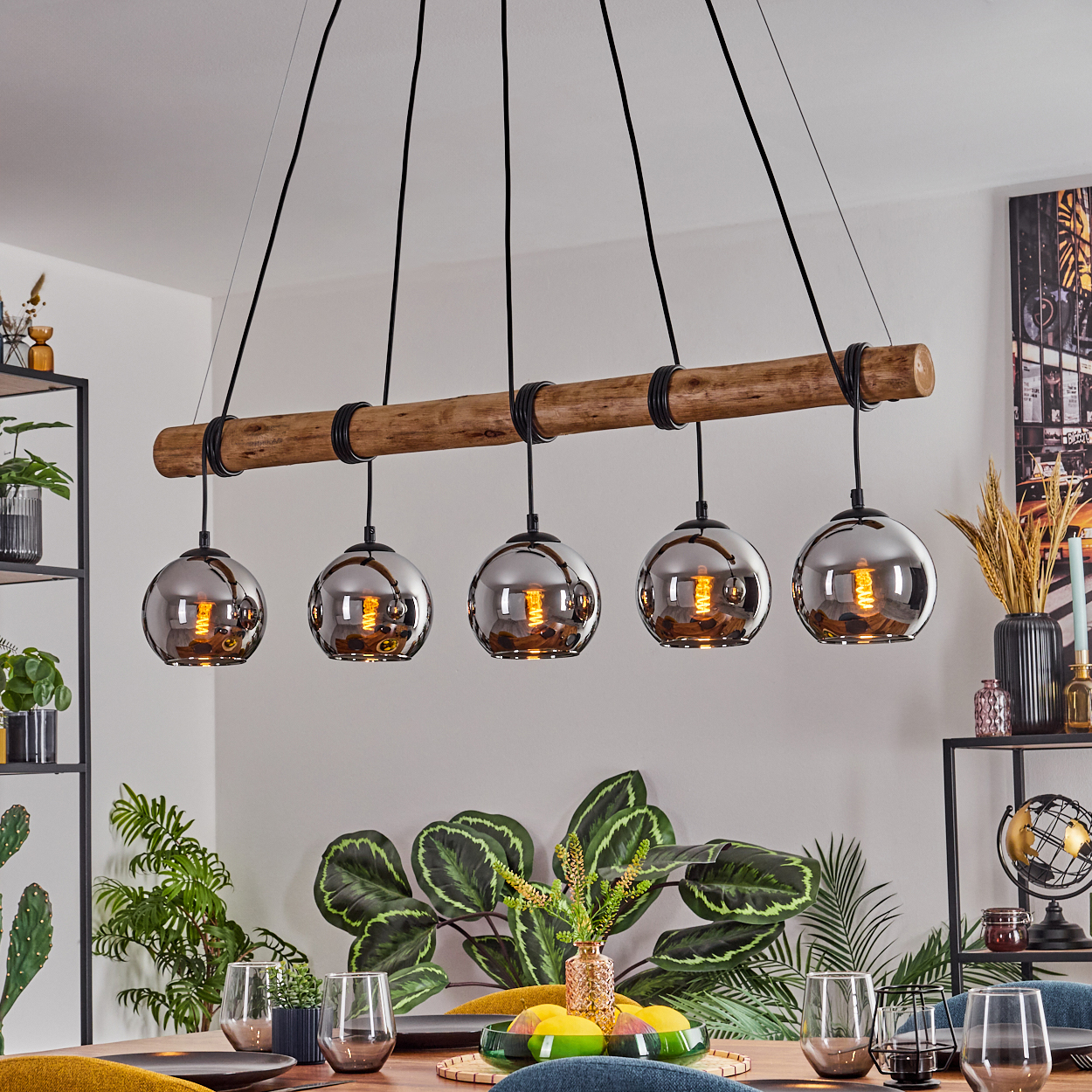 Ein Esszimmer mit Holztisch, Deckenleuchte mit fünf Pendelleuchten und dekorativen Pflanzen.