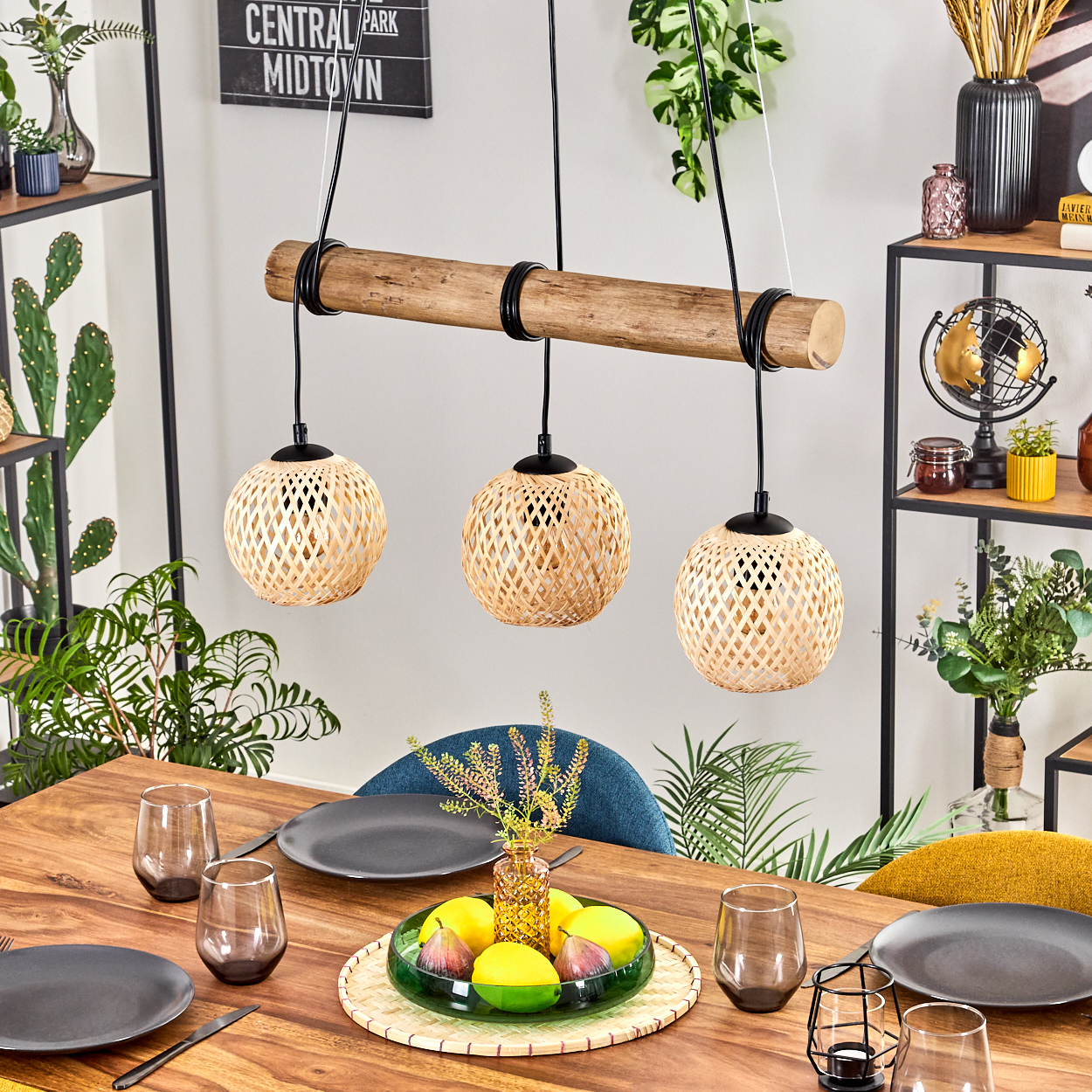 Esstisch mit Holzlampen. Früchte in grüner Schale. Pflanzen und Gläser auf dem Tisch.