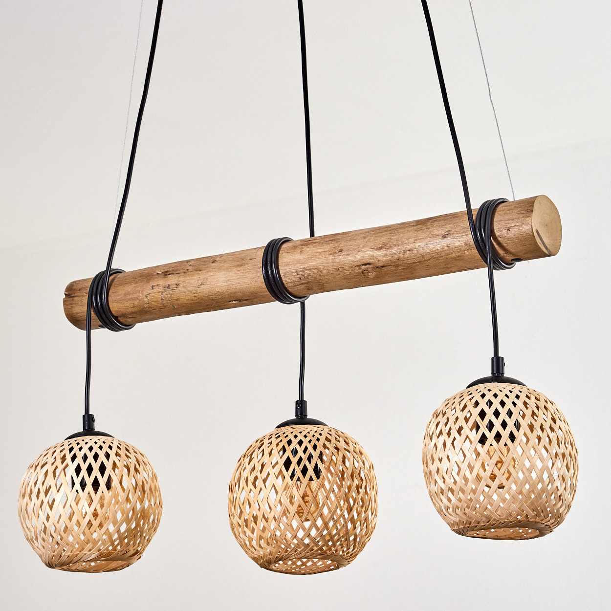 Ein Holzbalken mit drei hängenden gewebten Lampen. Die Lampen sind kugelförmig, der Balken wird von schwarzen Kabeln getragen.