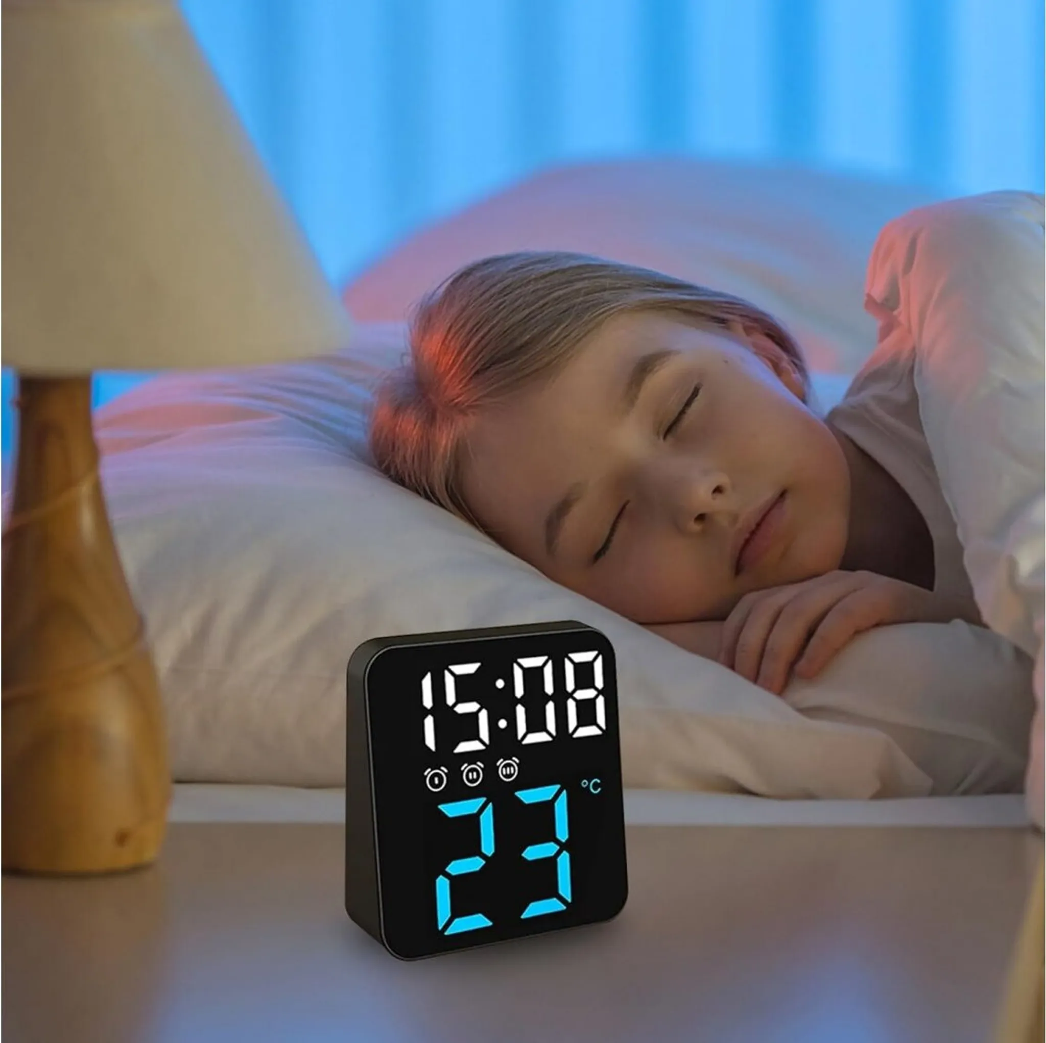 Ein schlafendes Mädchen im Bett. Eine Digitaluhr zeigt 15:08 und 23°C. Eine Lampe steht auf dem Nachttisch.
