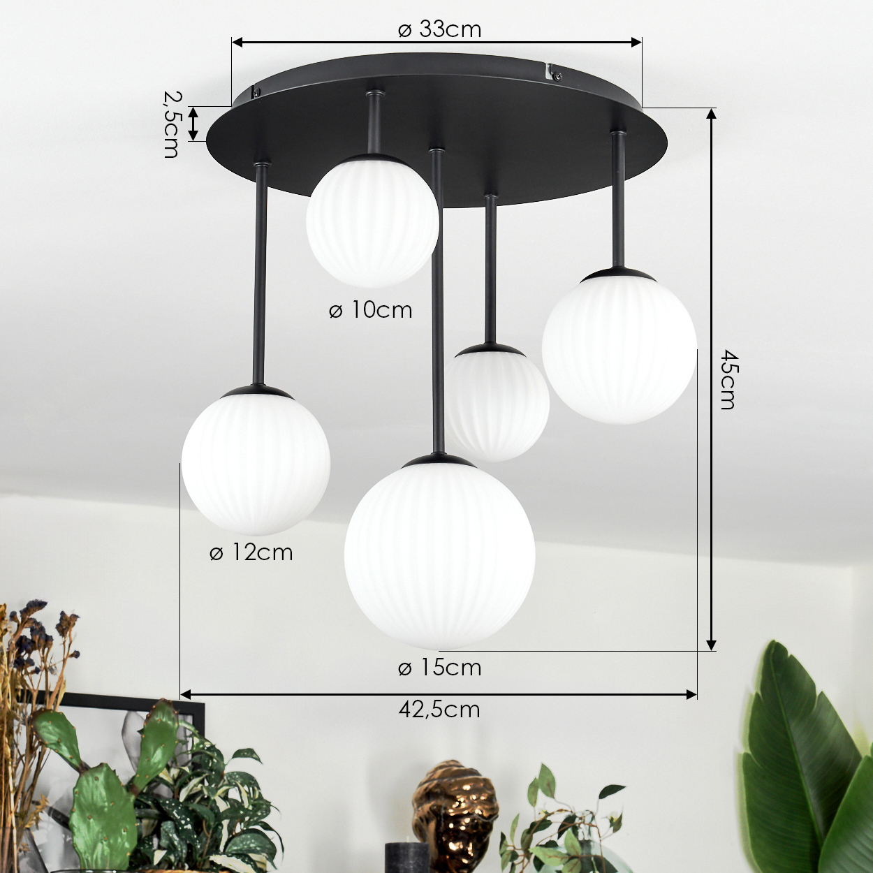 Moderne schwarze Deckenlampe mit fünf weißen Kugelleuchten. Maße sind angegeben. Pflanzen und Deko im Hintergrund.
