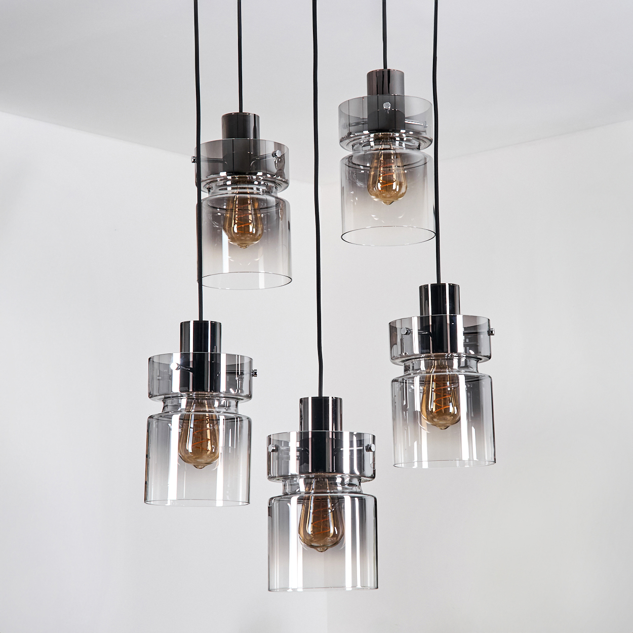 Fünf hängende Pendelleuchten mit Glasschirmen und Edison-Glühbirnen vor einer weißen Eckwand.
