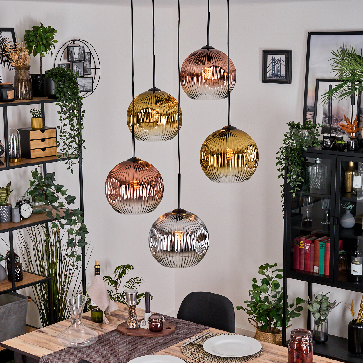 Esszimmer mit hängenden Kugelleuchten, Tisch mit Tellern und dekorativen Pflanzen. Rechts ein schwarzer Schrank.