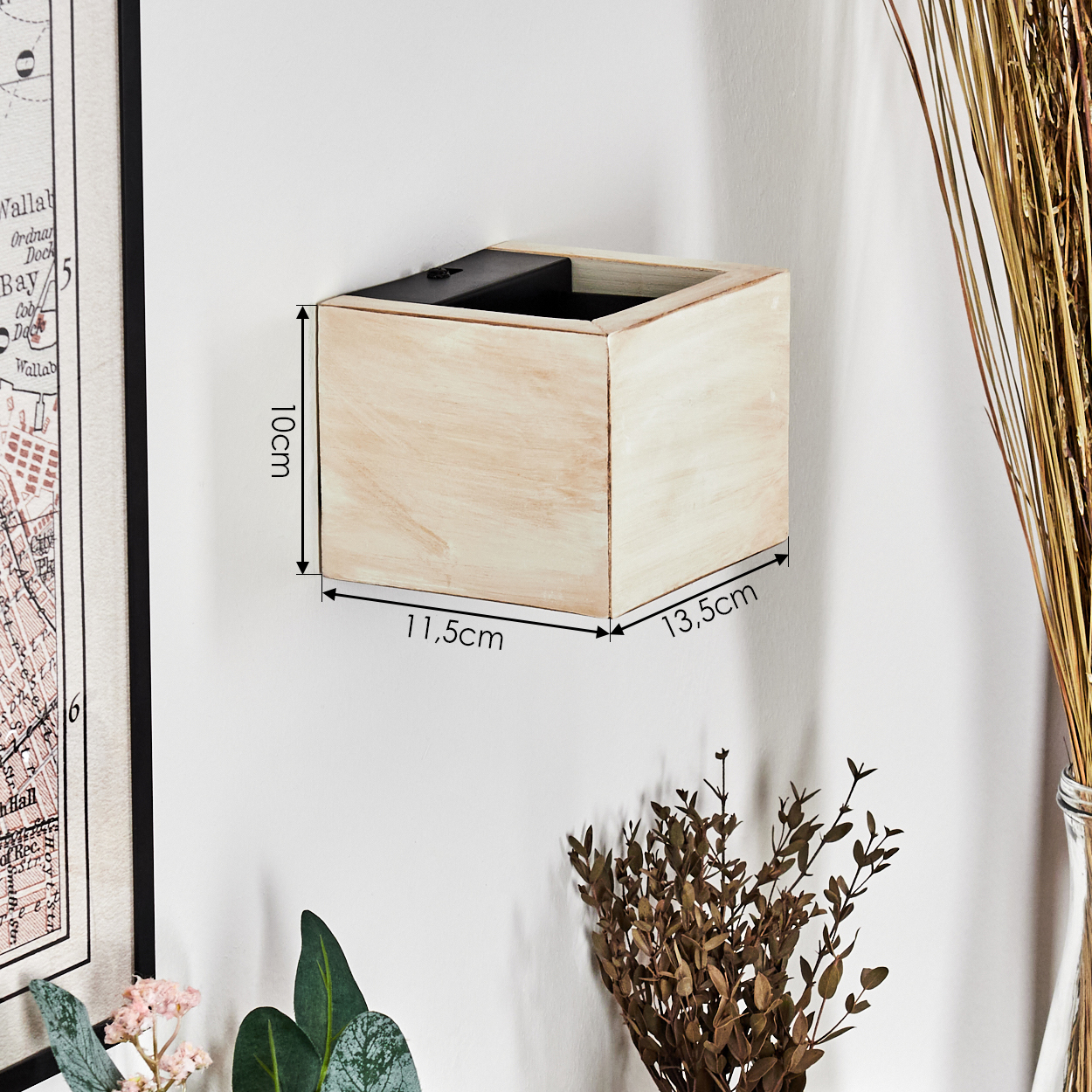 Eine beige Holzbox ist an einer weißen Wand montiert. Maße sind beschriftet: 10 cm, 11,5 cm und 13,5 cm. Dekorative Pflanzen im Hintergrund.