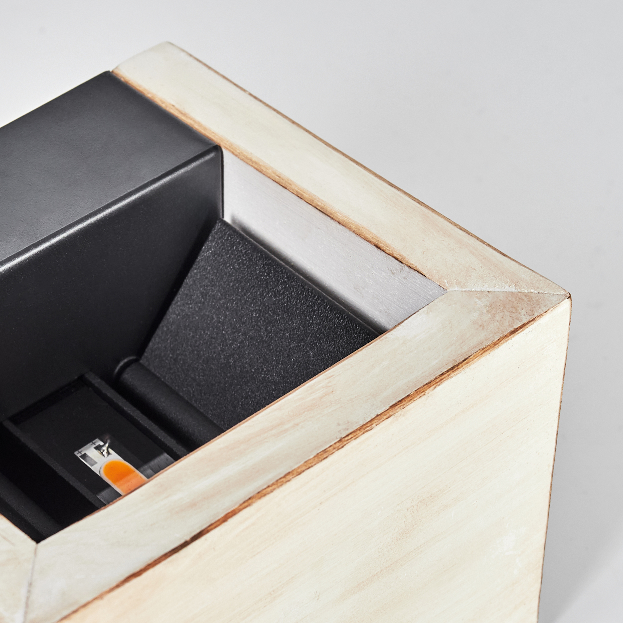 Nahaufnahme einer Holzkiste. Im Inneren der Kiste befinden sich schwarze und graue Oberflächen. Ein orange-weißes Etikett befindet sich in der Kiste.