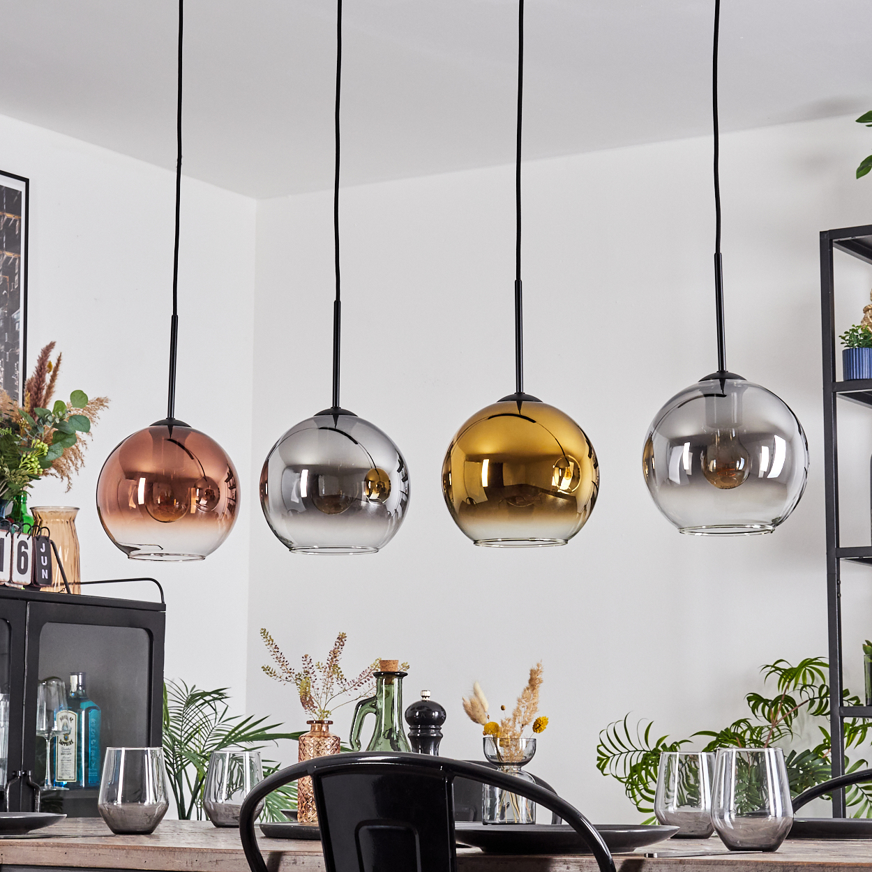 Vier kugelförmige Pendelleuchten in Kupfer, Silber, Gold und Silber. Darunter ein Esstisch. Dekorative Gegenstände sind vorhanden.