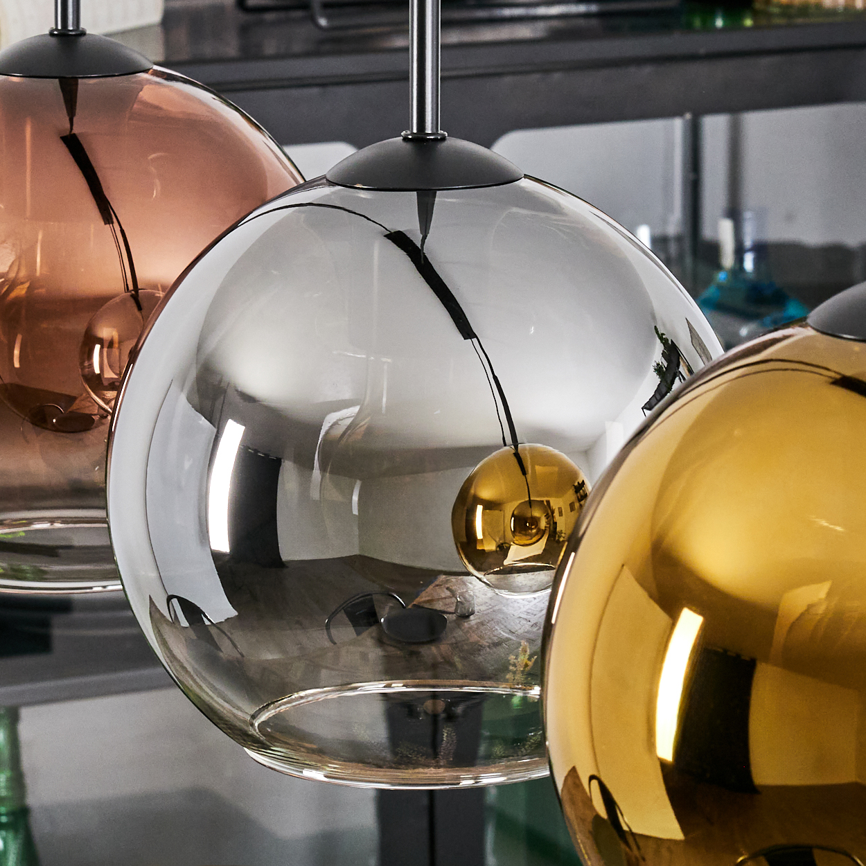 Drei kugelförmige Pendelleuchten in Kupfer, Silber und Gold. Die Leuchten spiegeln die Details des Raumes wider und schaffen ein modernes Interieur.
