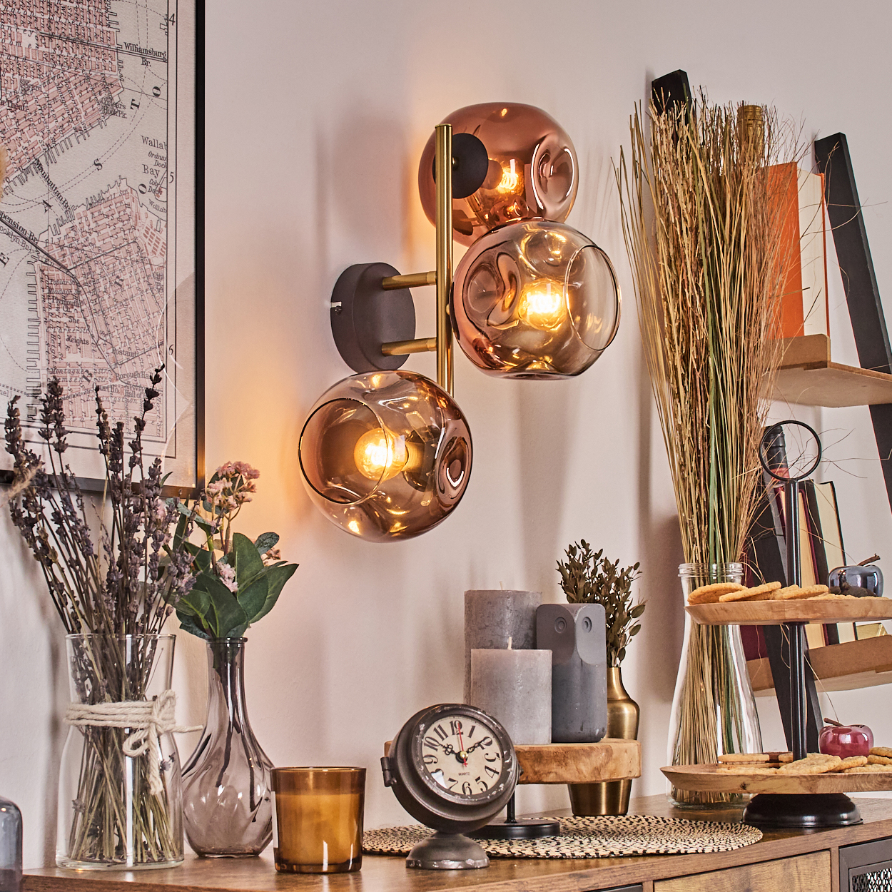 Ein Raum mit Wandlampe, Uhr, Blumen, Kerzen und einem Regal mit Keksen und Äpfeln auf einem Holztisch.