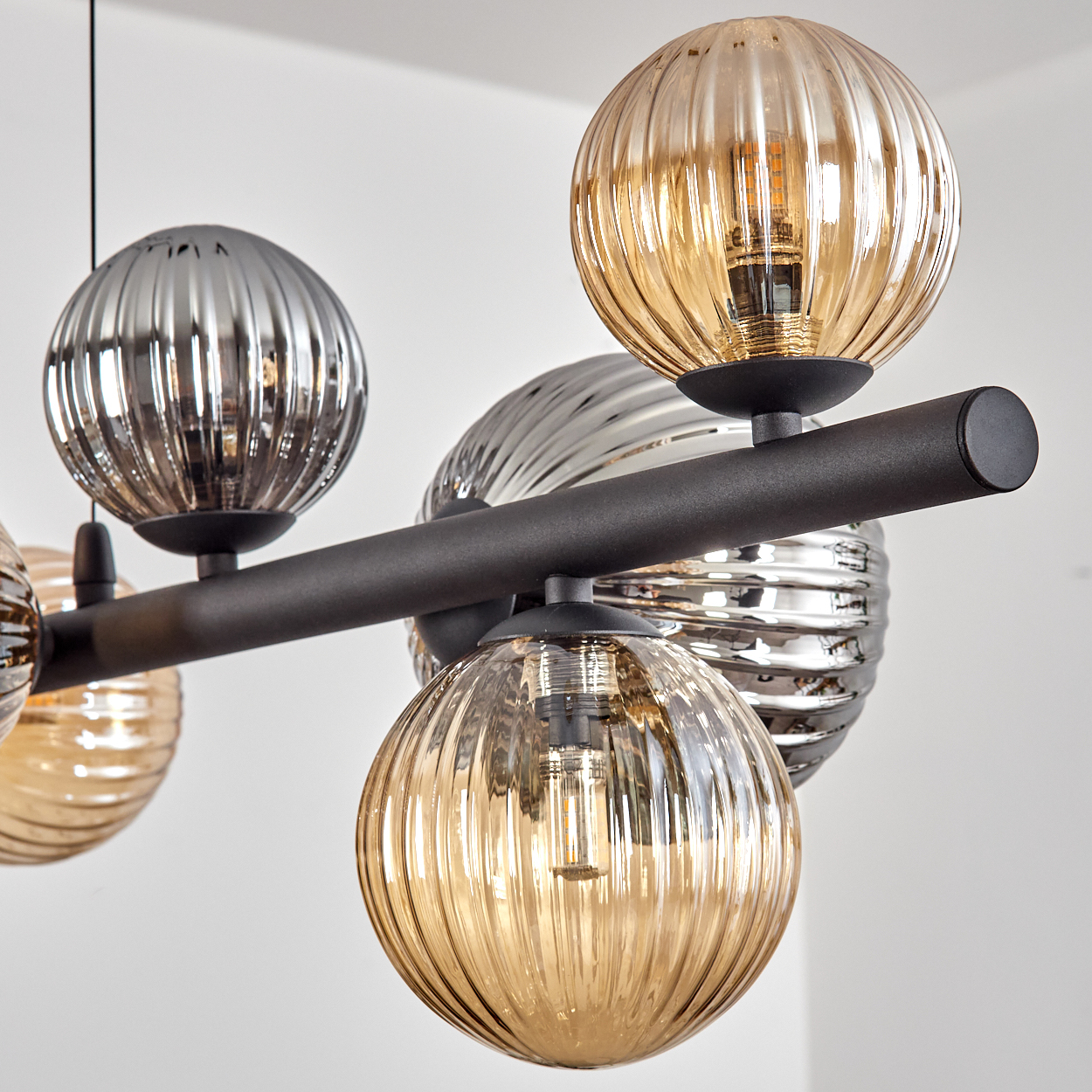 Nahaufnahme einer modernen Deckenleuchte mit kugelförmigen, gerippten Glasschirmen in Bernstein- und Silbertönen, mit schwarzen Metallarmen.