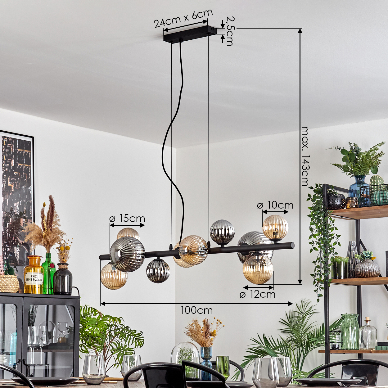 Eine moderne schwarze Pendelleuchte mit Glaskugeln hängt über einem Esstisch, der für eine Mahlzeit gedeckt ist. Der Hintergrund zeigt Regale und Pflanzen.