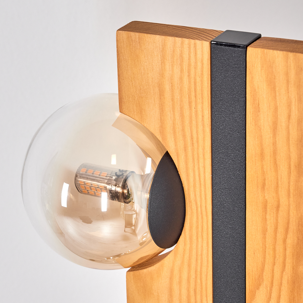 Nahaufnahme einer Lampe mit runder Glühbirne, Holzelementen und einem schwarzen Metallstreifen vor weißem Hintergrund.