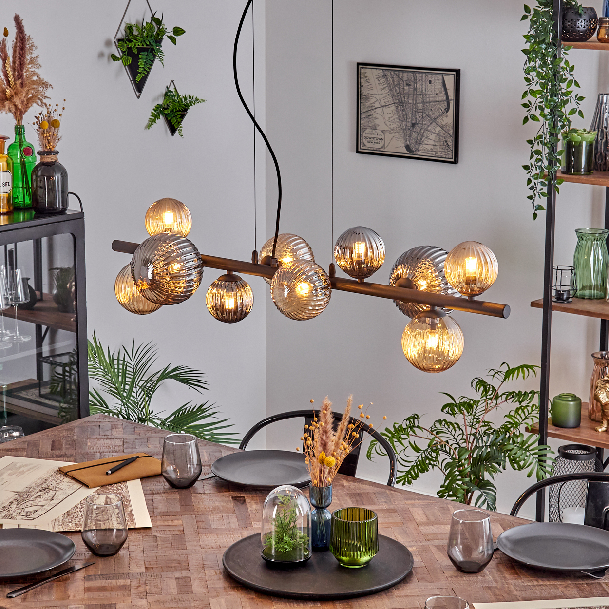 Esszimmer mit einem Holztisch mit Tellern, Gläsern und Dekorationen. Eine moderne Hängelampe hängt über dem Tisch.