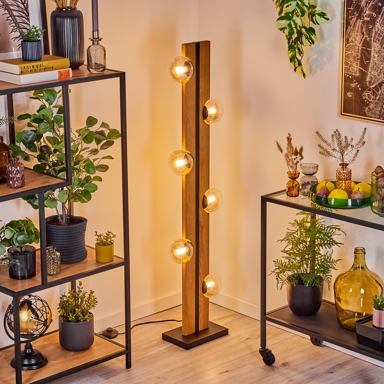 Ein modernes Wohnzimmer mit einer Holzlampe, Regalen mit Pflanzen und Büchern sowie einem Beistelltisch mit Pflanzen und Obst.