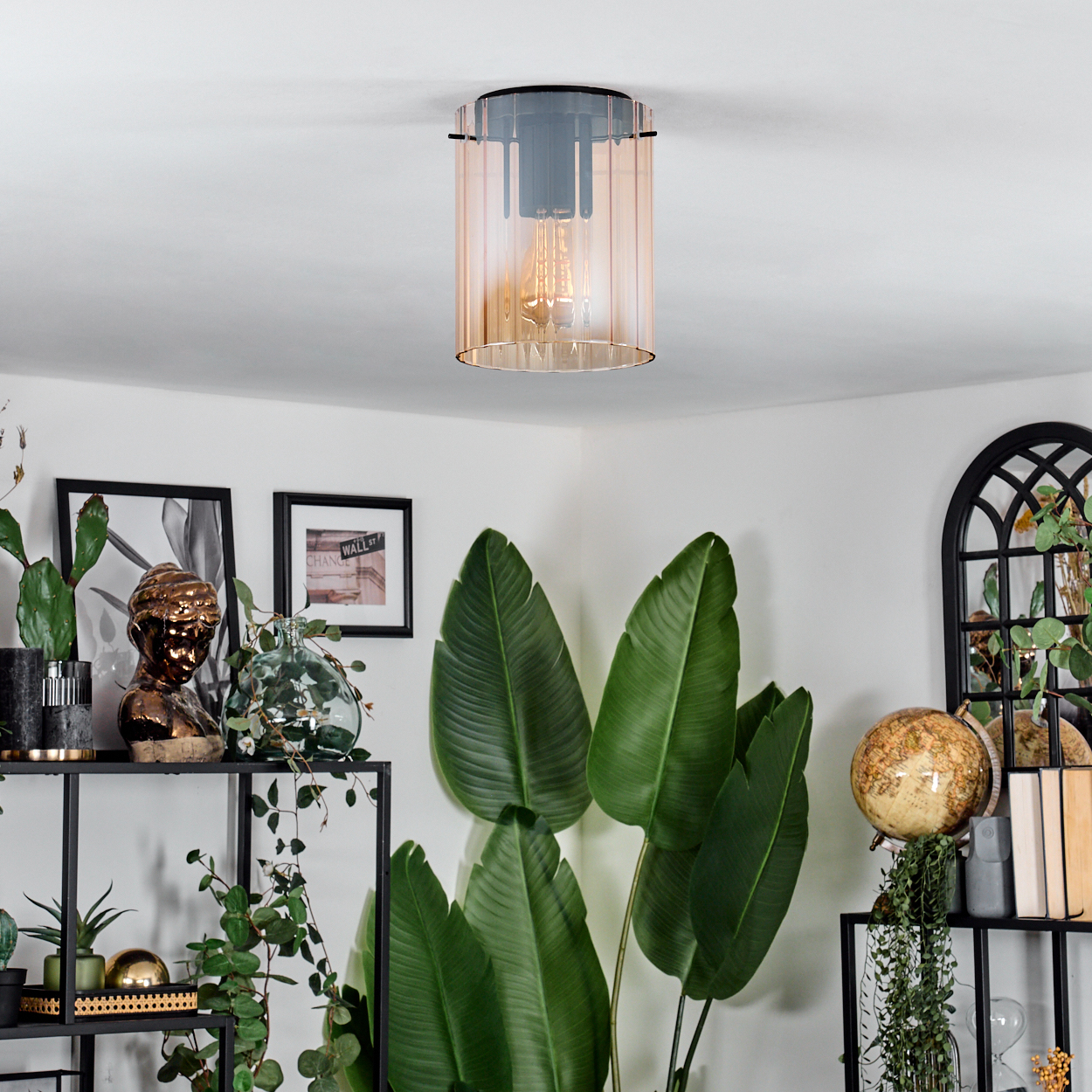 Eine moderne Leuchte hängt von der Decke. Darunter ist ein Raum mit Pflanzen, Bildern und einem Globus dekoriert.